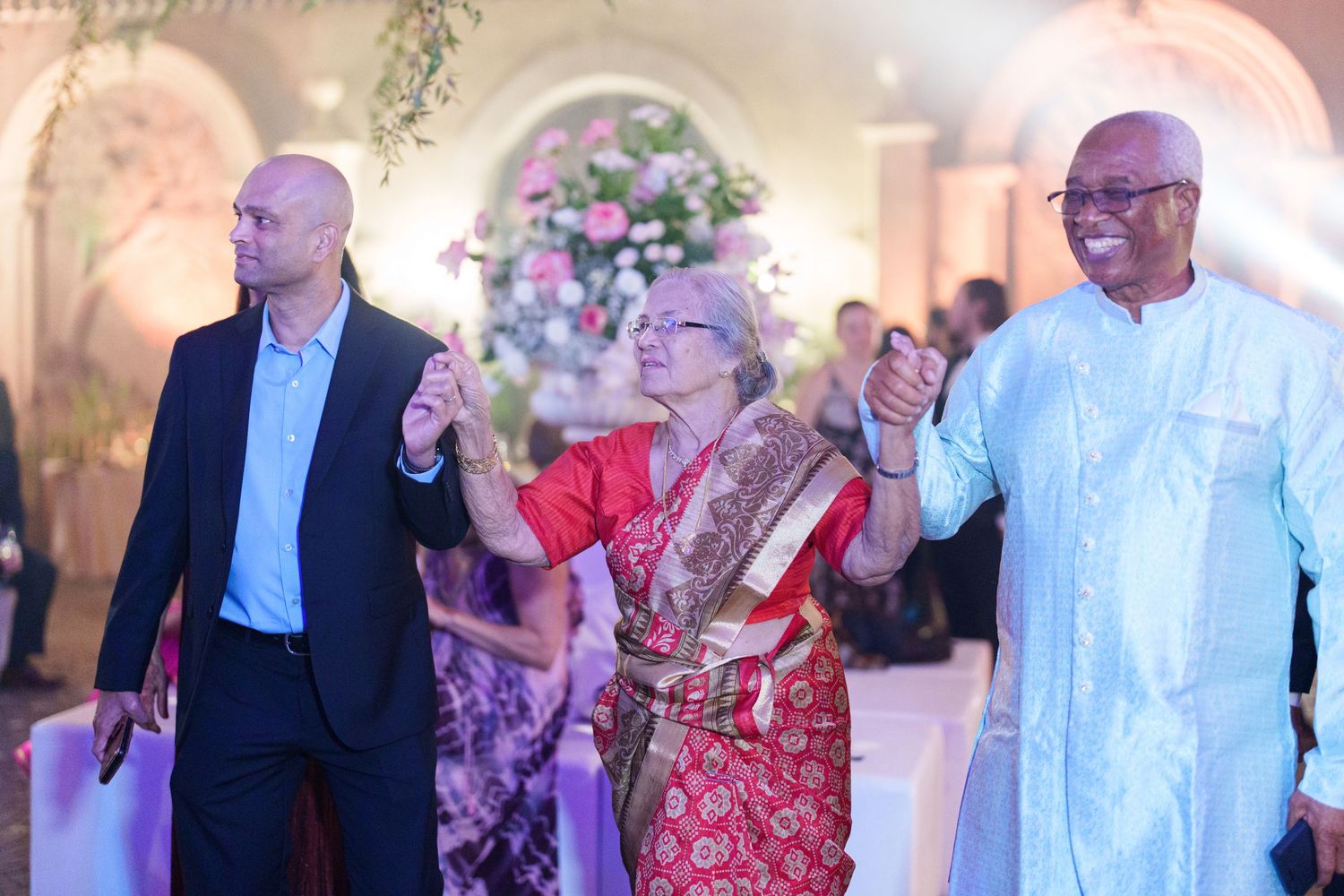 Wedding guests in formal attire mingle and celebrate at an elegantly lit indoor reception.