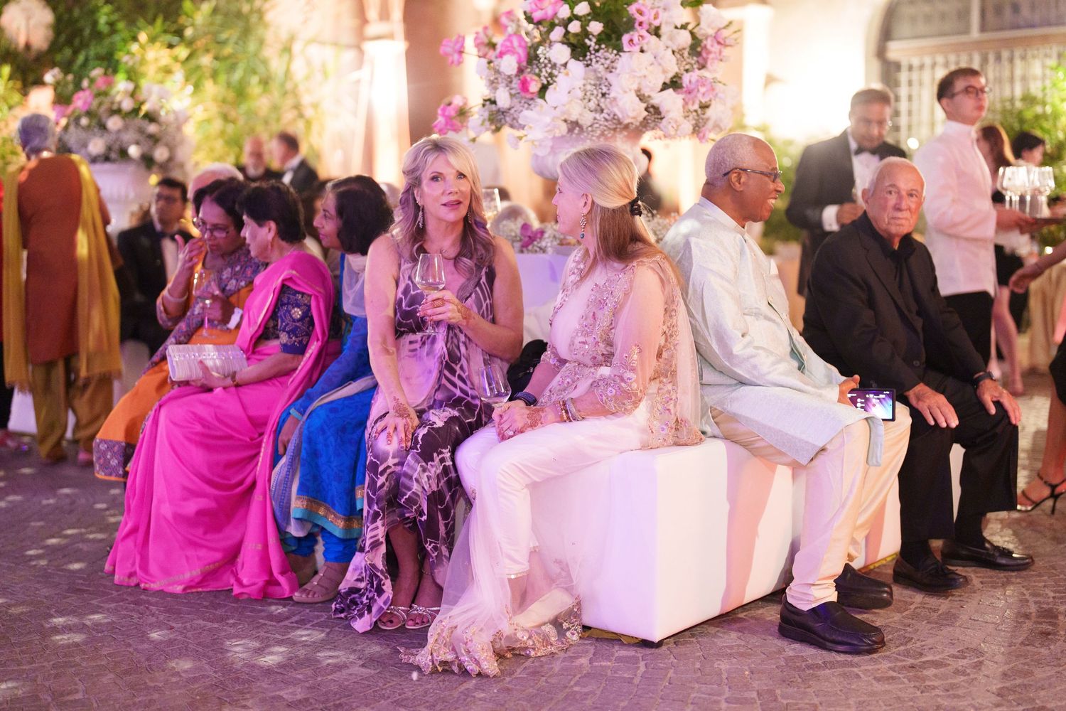 Wedding reception guests enjoy an elegant evening celebration with colorful mood lighting and white decor.