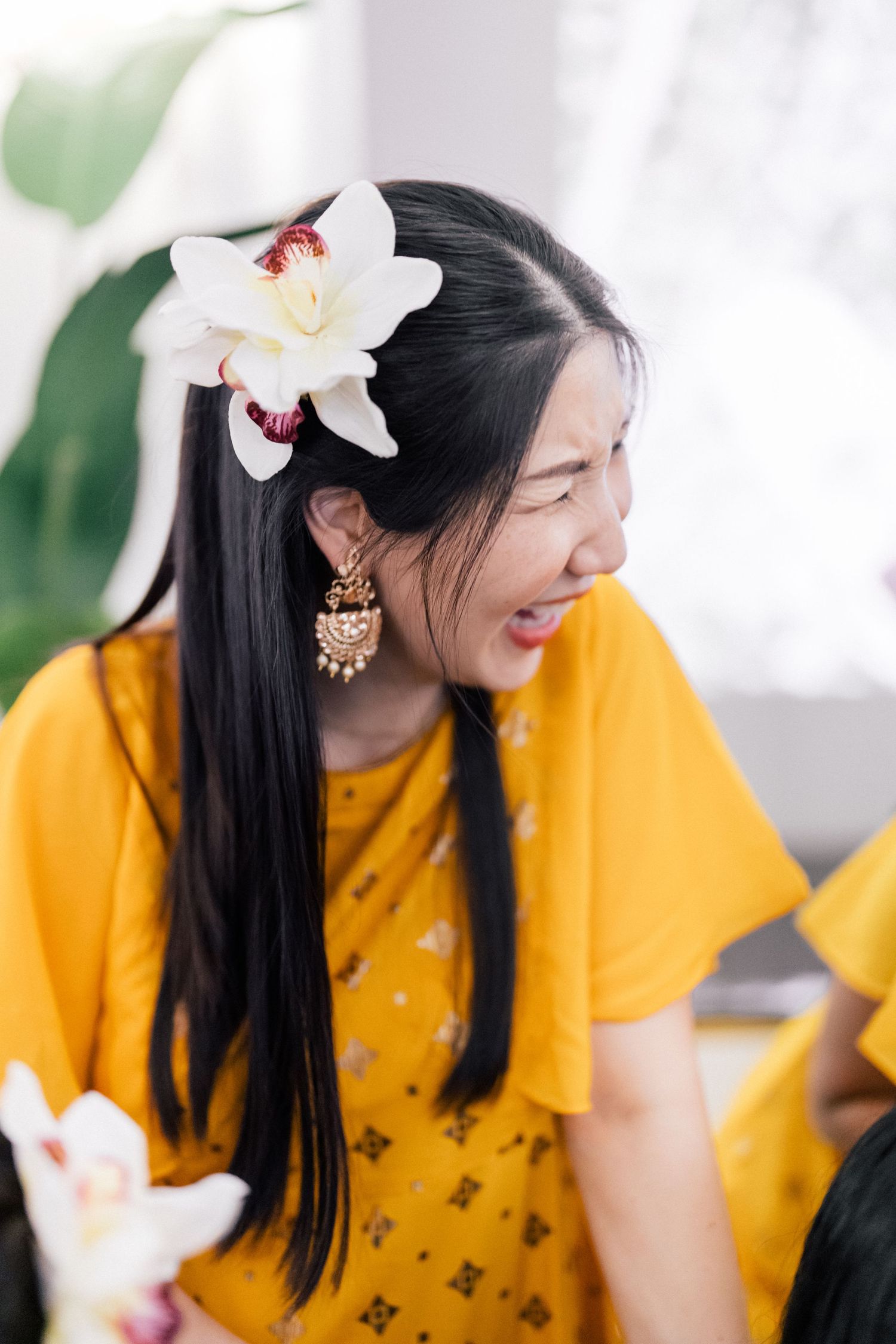 Person in yellow dress with white orchid hair accessory laughing during celebration.