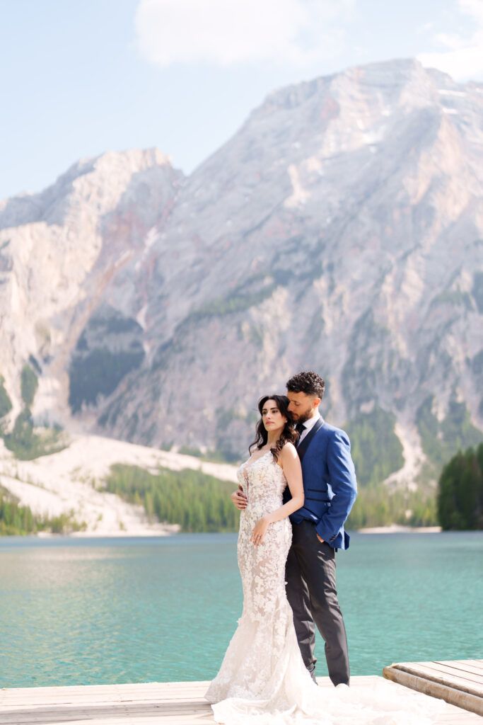 Wedding photography session on a dock overlooking turquoise alpine lake and mountain peaks.