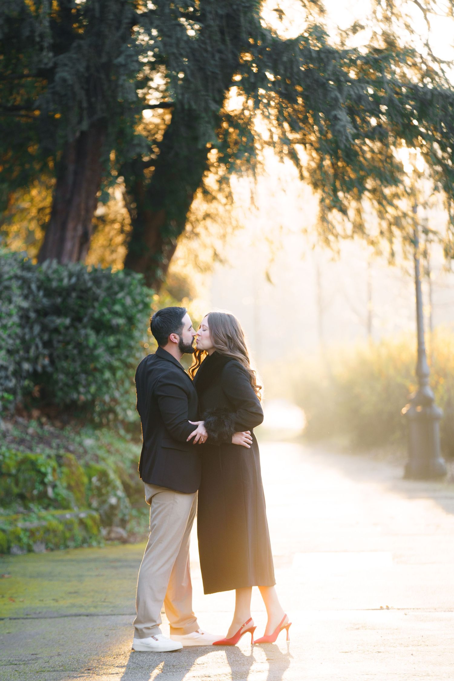 A couple shares a romantic moment on a misty path during golden hour as sunlight filters through the trees.