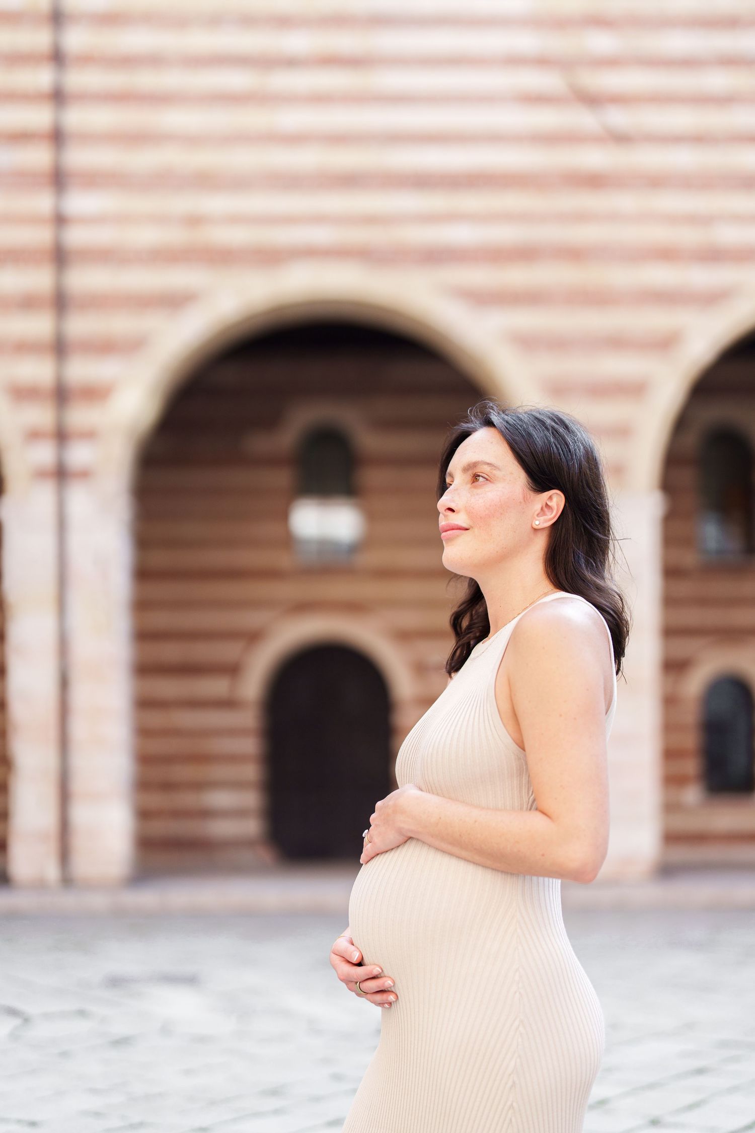 Woman in cream colored dress spins gracefully in an outdoor plaza with arched architecture in the background.