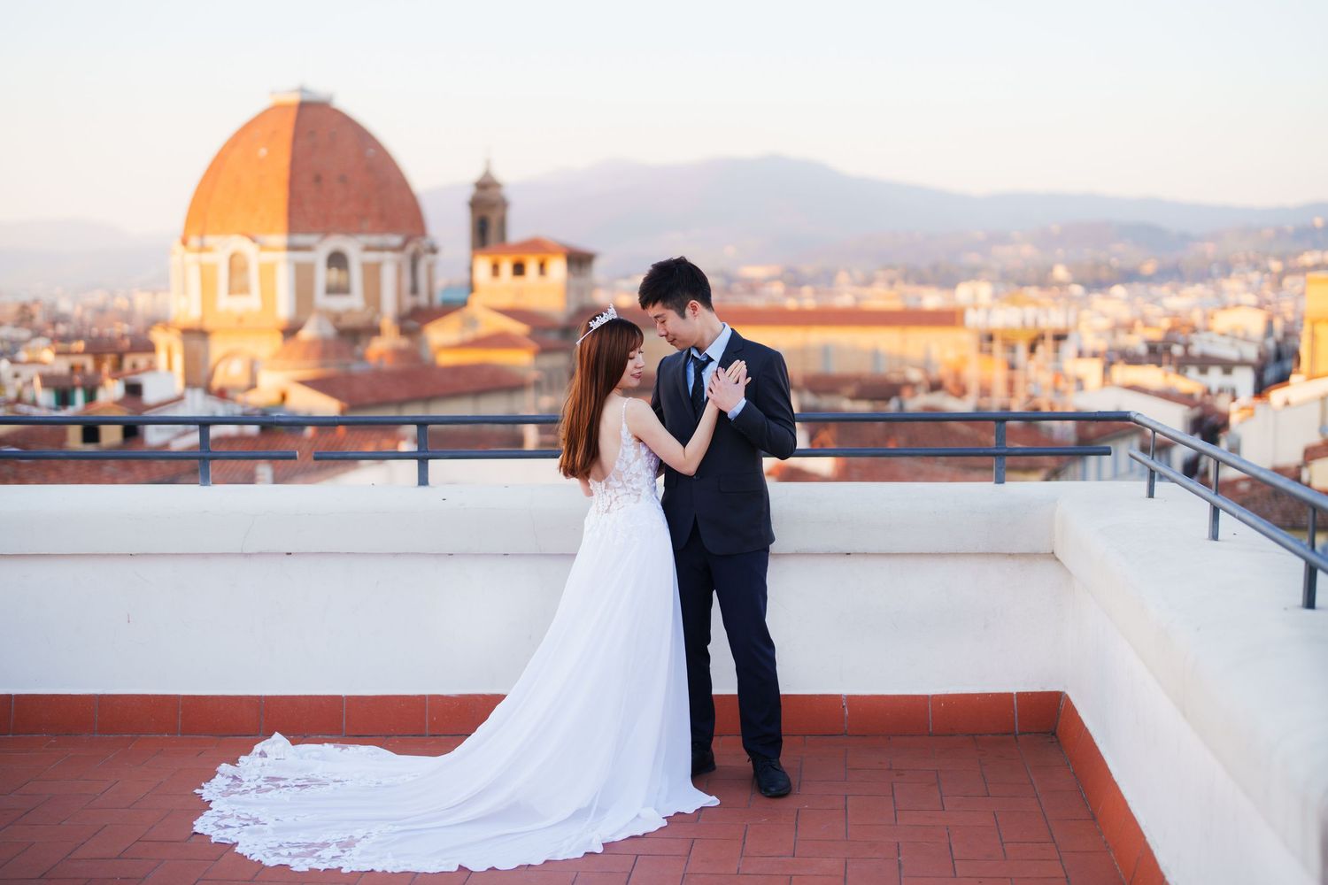A couple in wedding attire embraces on a rooftop terrace overlooking Florence with the Duomo cathedral in the background.