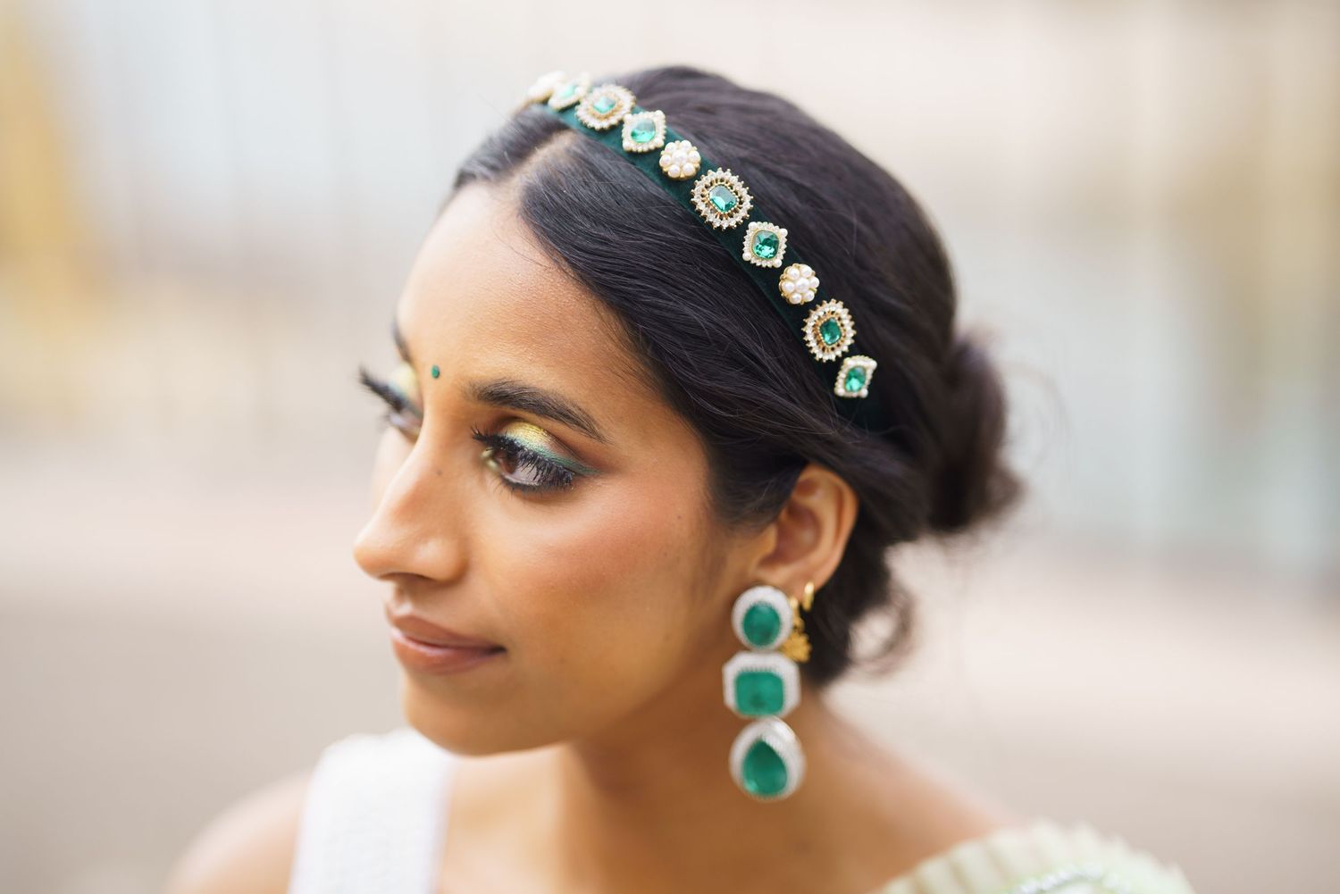 Indian bride wearing traditional emerald green and gold jewelry with matching headpiece and earrings.