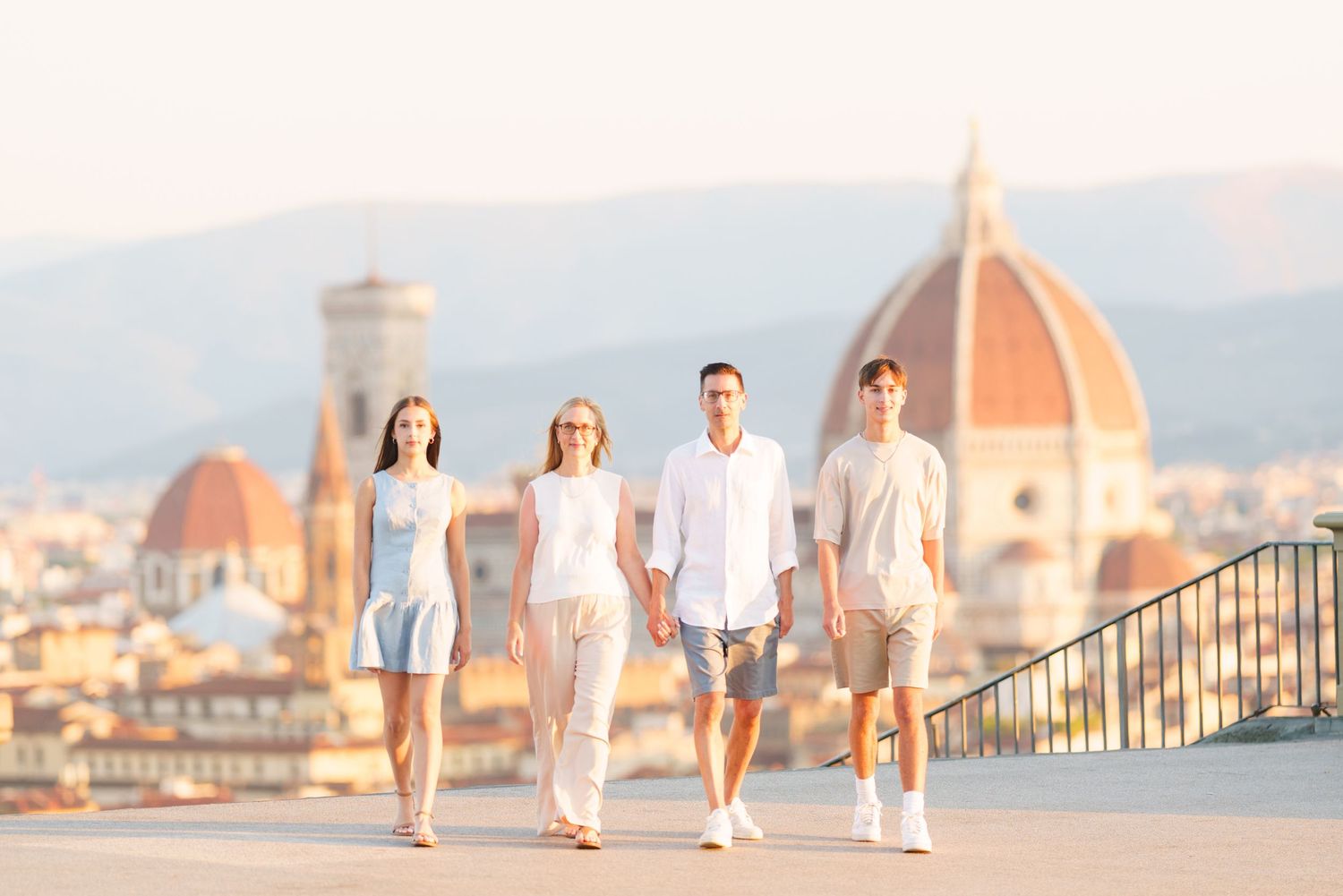 Family walking along a scenic overlook with Florence's Duomo cathedral and cityscape in the background at sunset.
