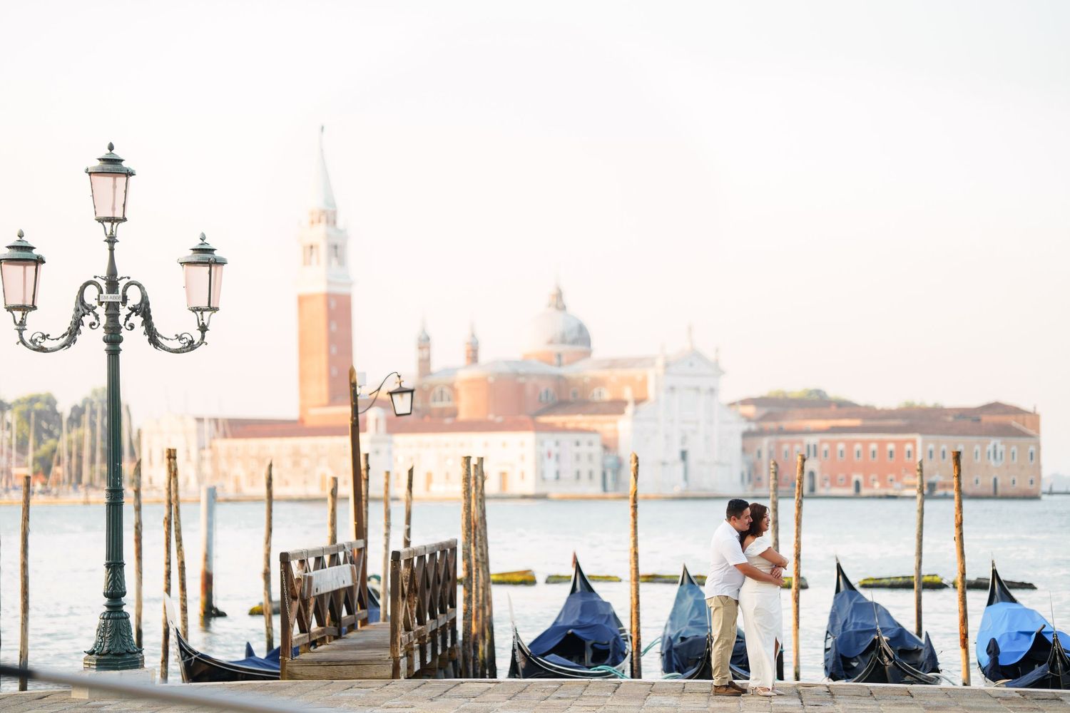 A panoramic view of Venice's waterfront with traditional lamp posts and the iconic San Giorgio Maggiore church in the distance.