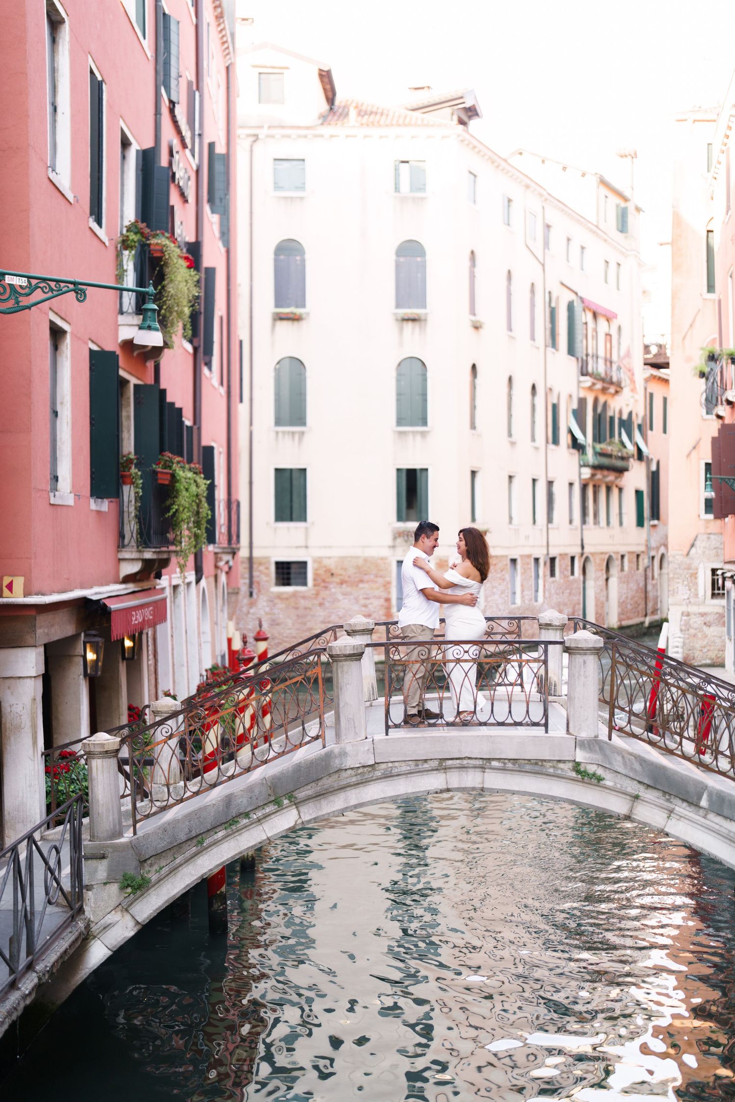 A picturesque view of a narrow Venetian canal with traditional bridges, pink buildings, and reflective water.
