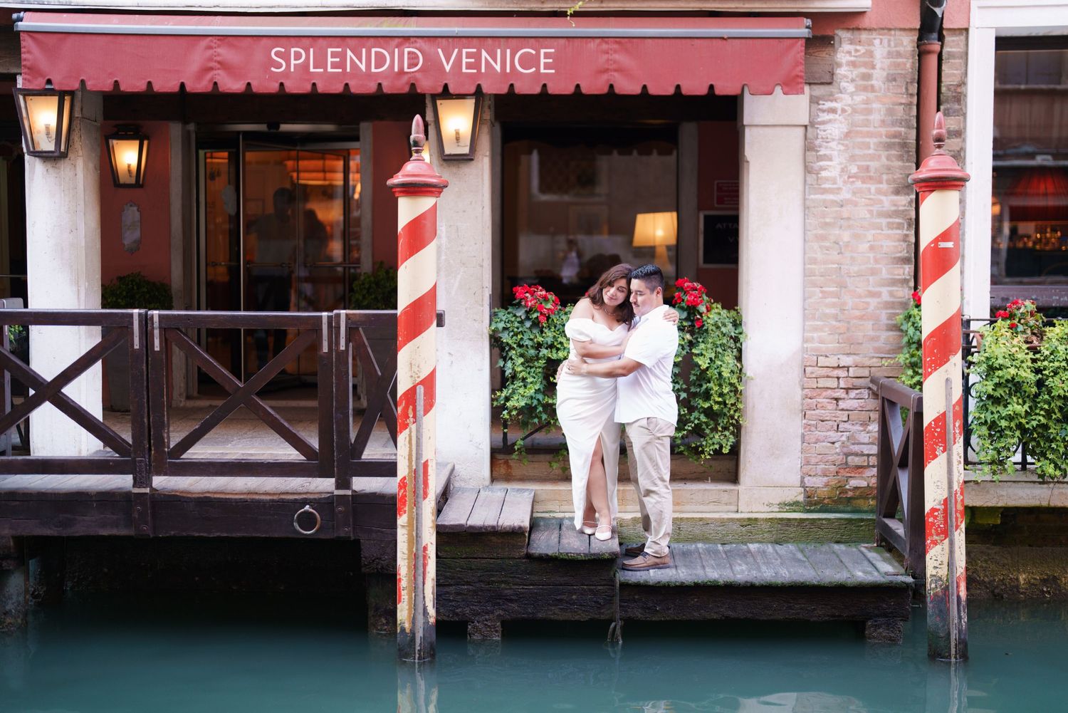 A row of iconic red and white striped mooring poles line a Venetian canal next to traditional buildings and walkways.