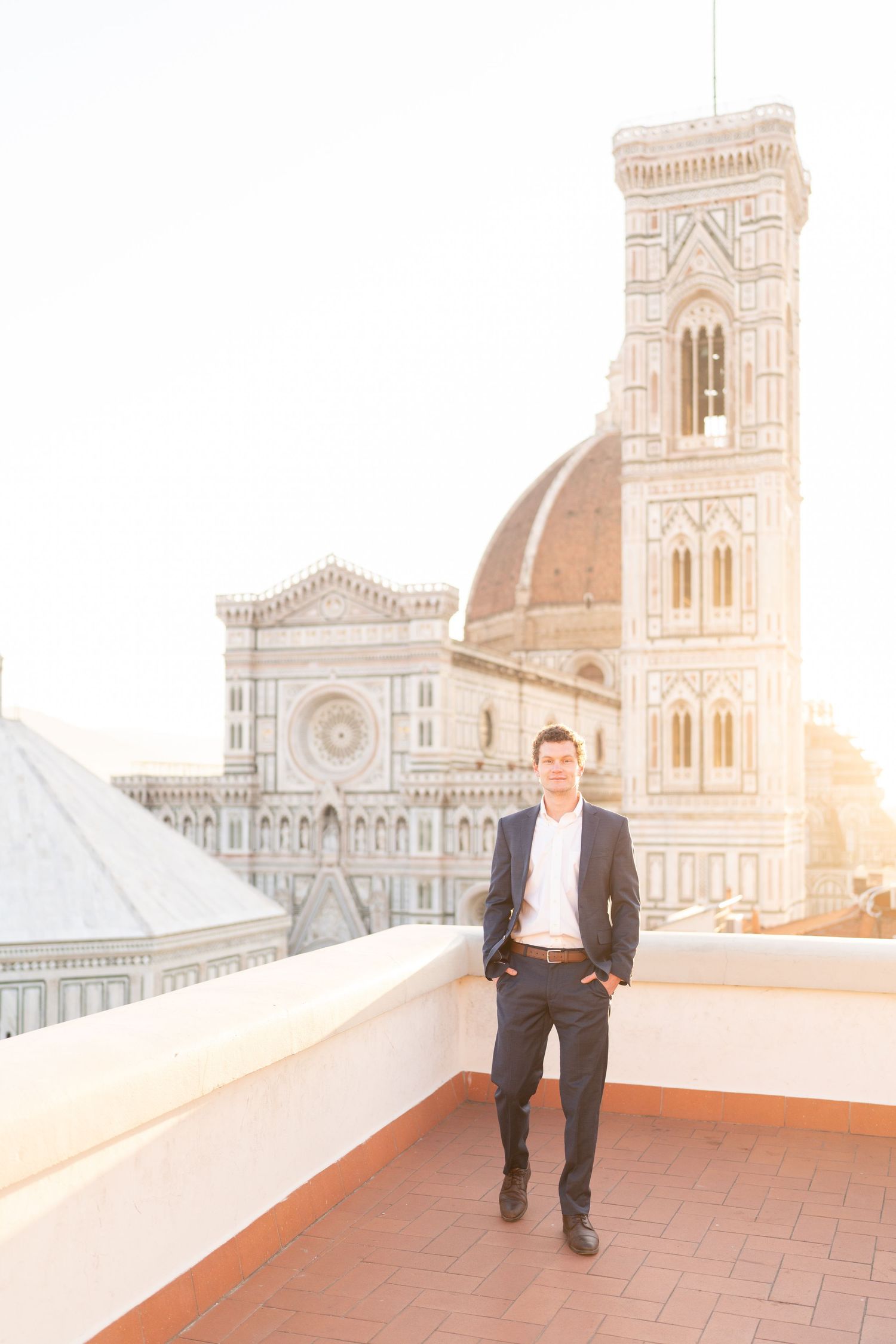 A person stands on a terrace overlooking the historic Duomo cathedral in Florence, Italy during golden hour.