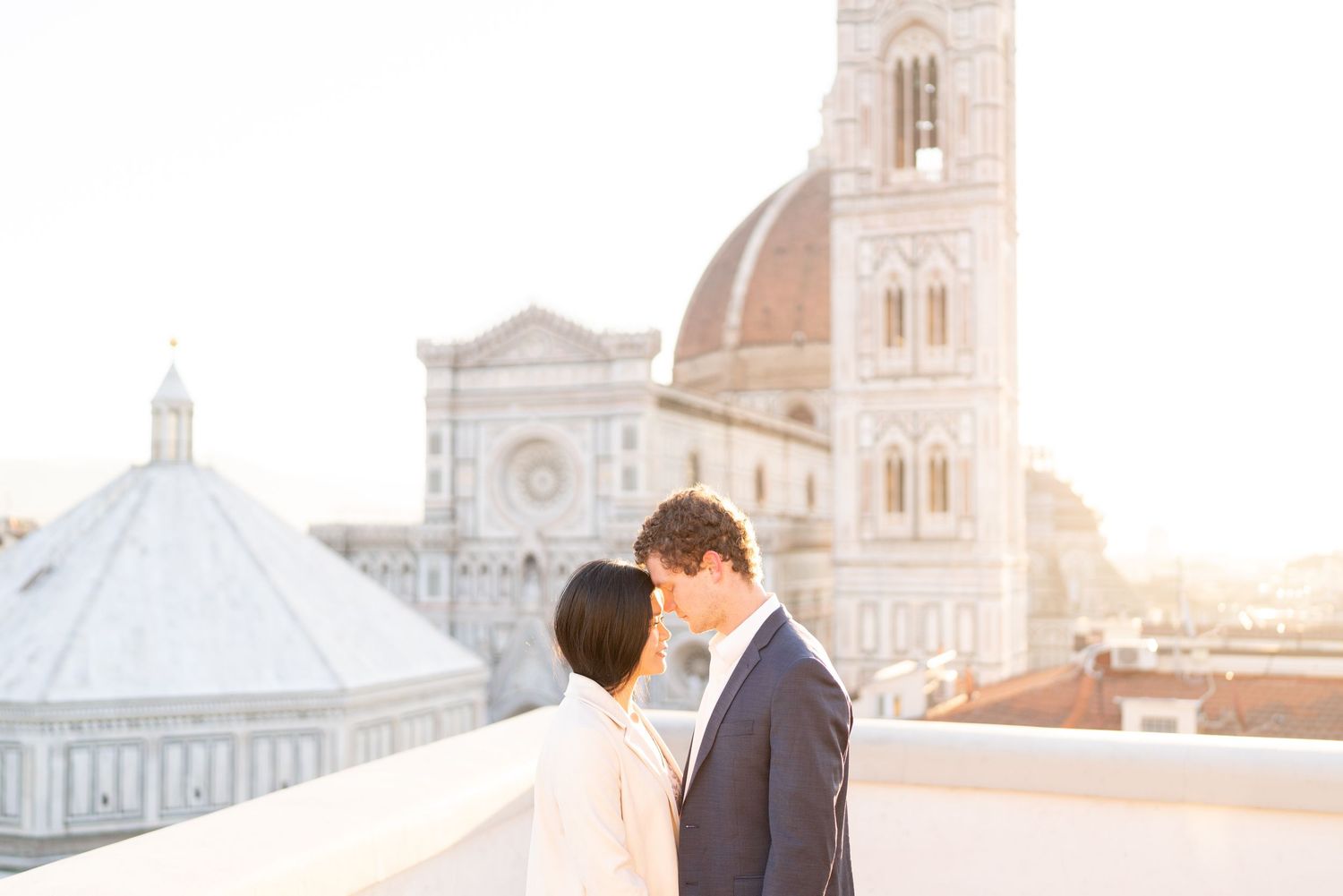 A romantic couple shares a tender moment at sunset in Florence, Italy with the Duomo cathedral visible in the background.