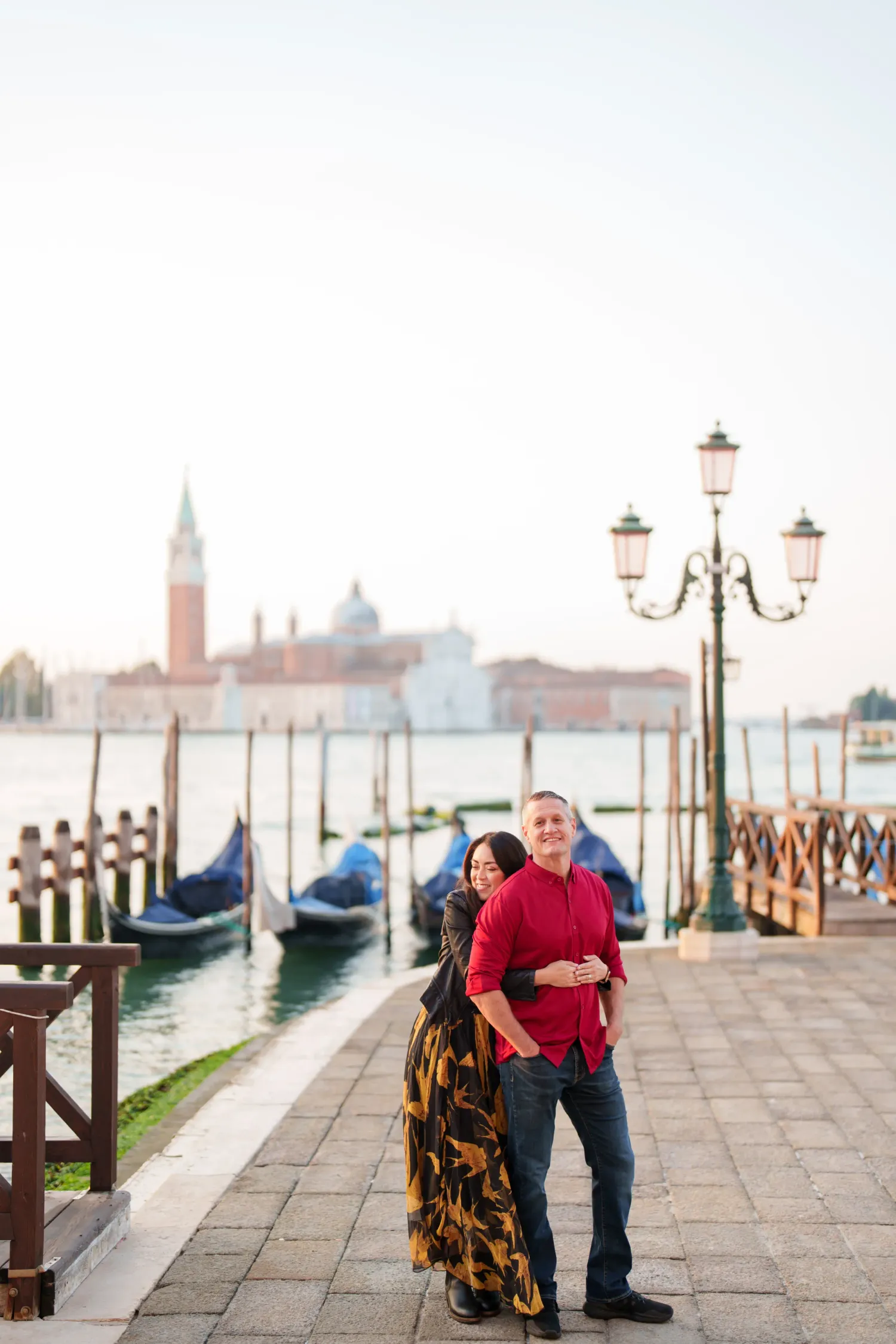 Romantic couple shares tender moments along Venice's waterfront with gondolas and historic architecture in the background.