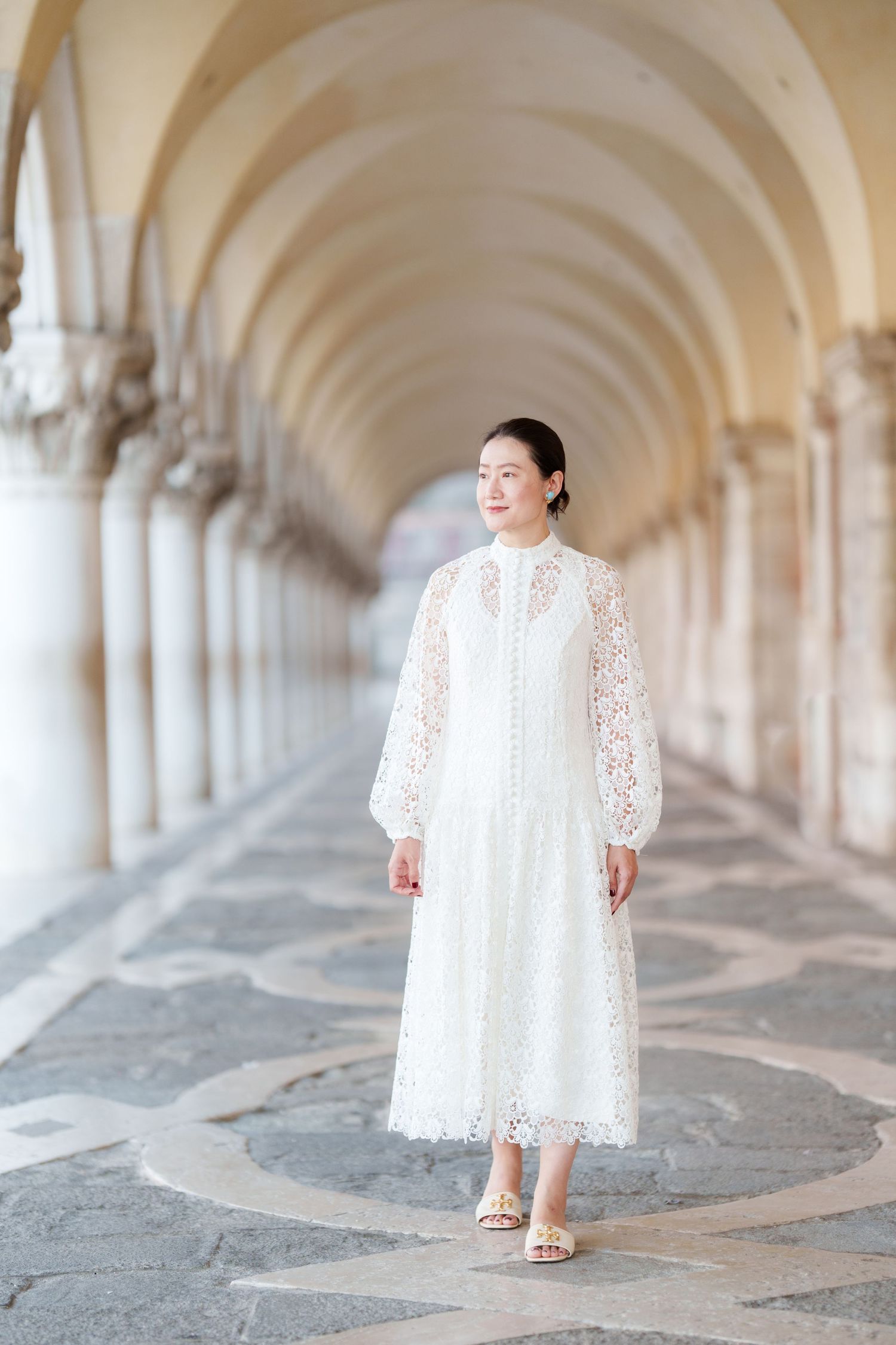 Woman in white lace midi dress walking under arched colonnade in Venice, Italy.