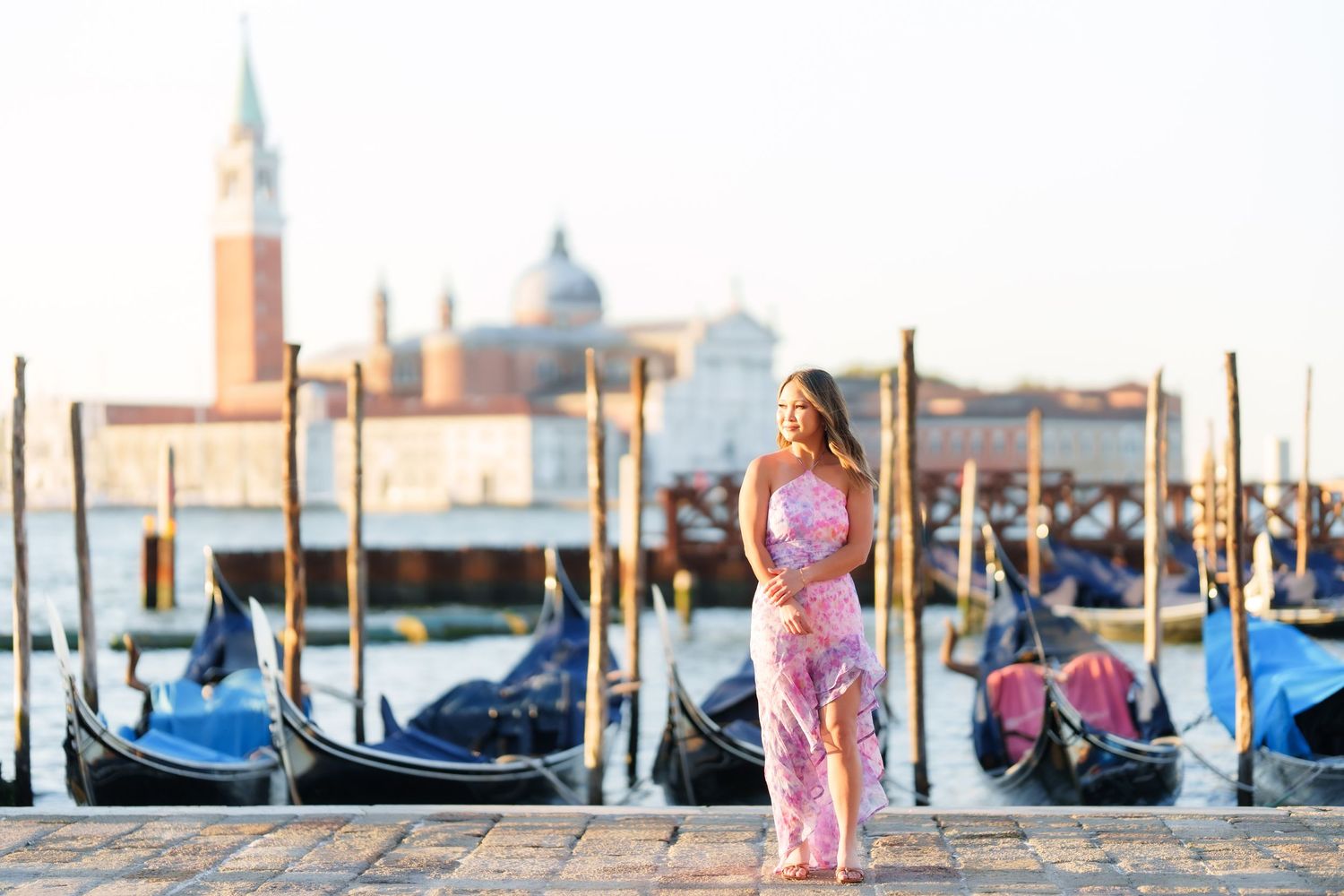 Woman in pink dress poses by Venice gondolas with San Giorgio Maggiore island in the background.