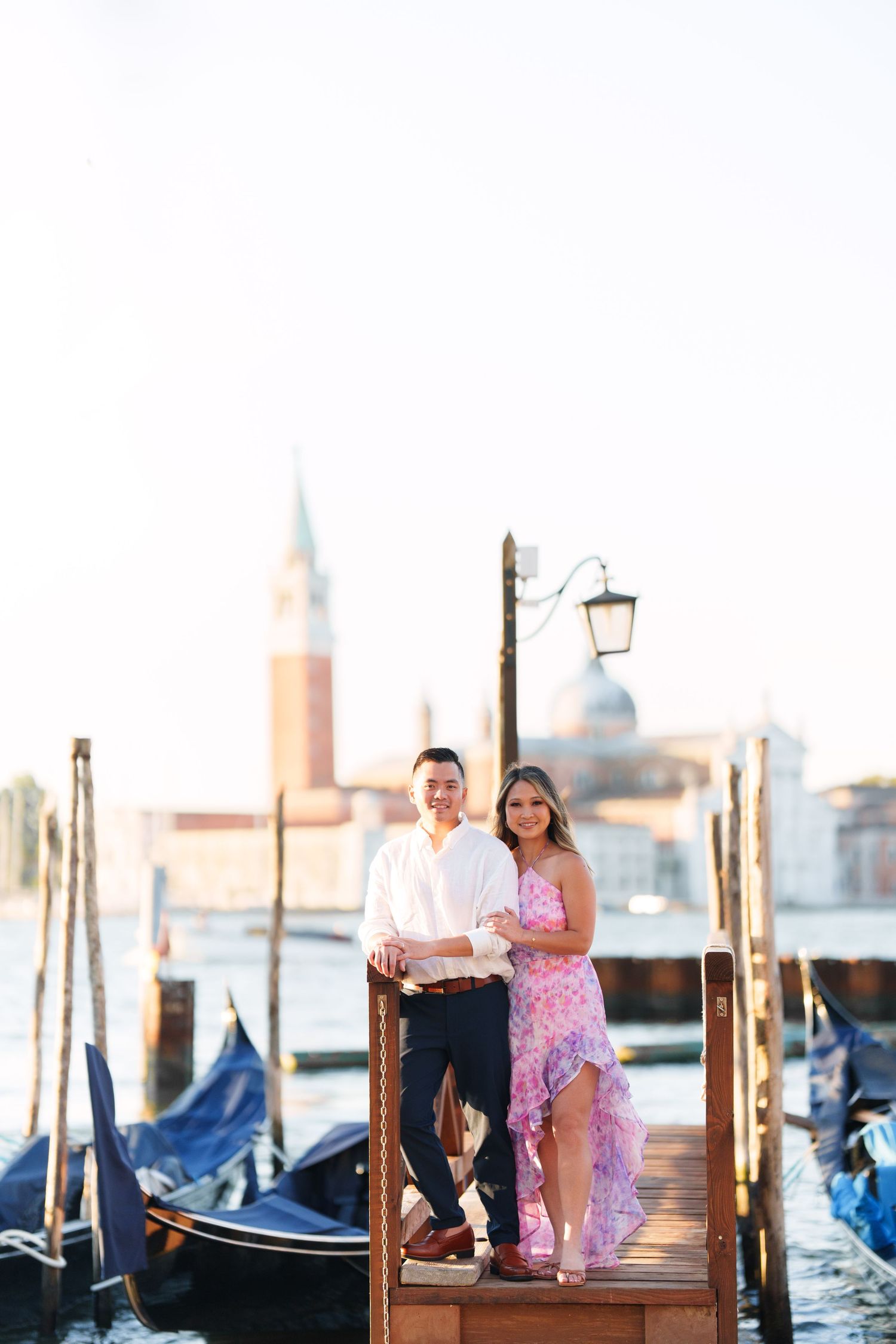 Couple posing on a Venice gondola dock with San Giorgio Maggiore church and gondolas in the background.