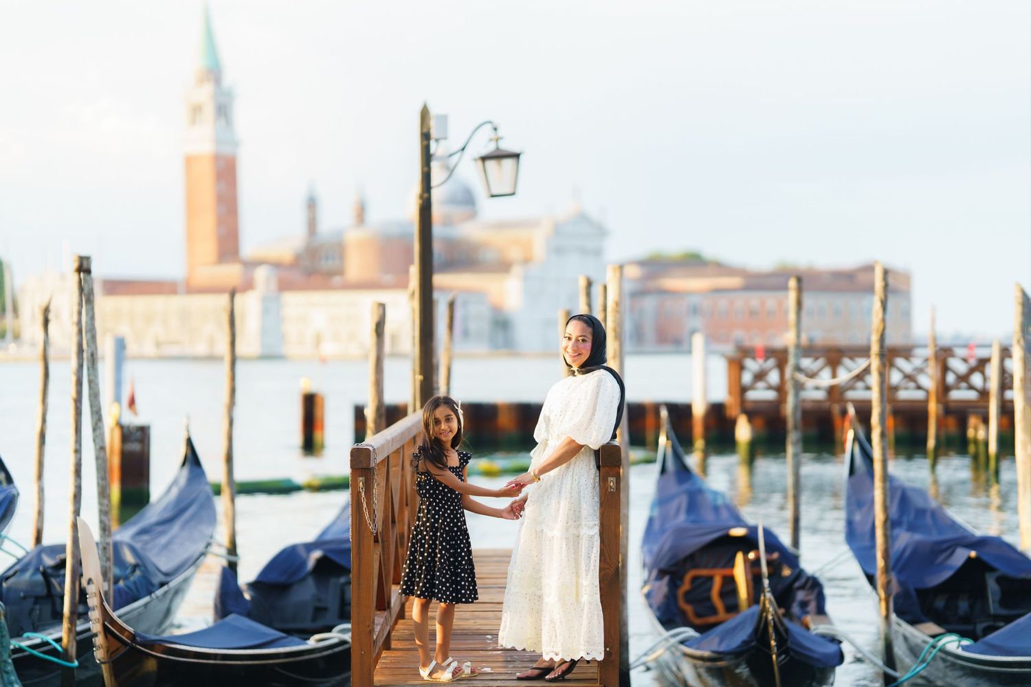 A mother and daughter stand on a Venice dock surrounded by gondolas with San Giorgio Maggiore island in the background.
