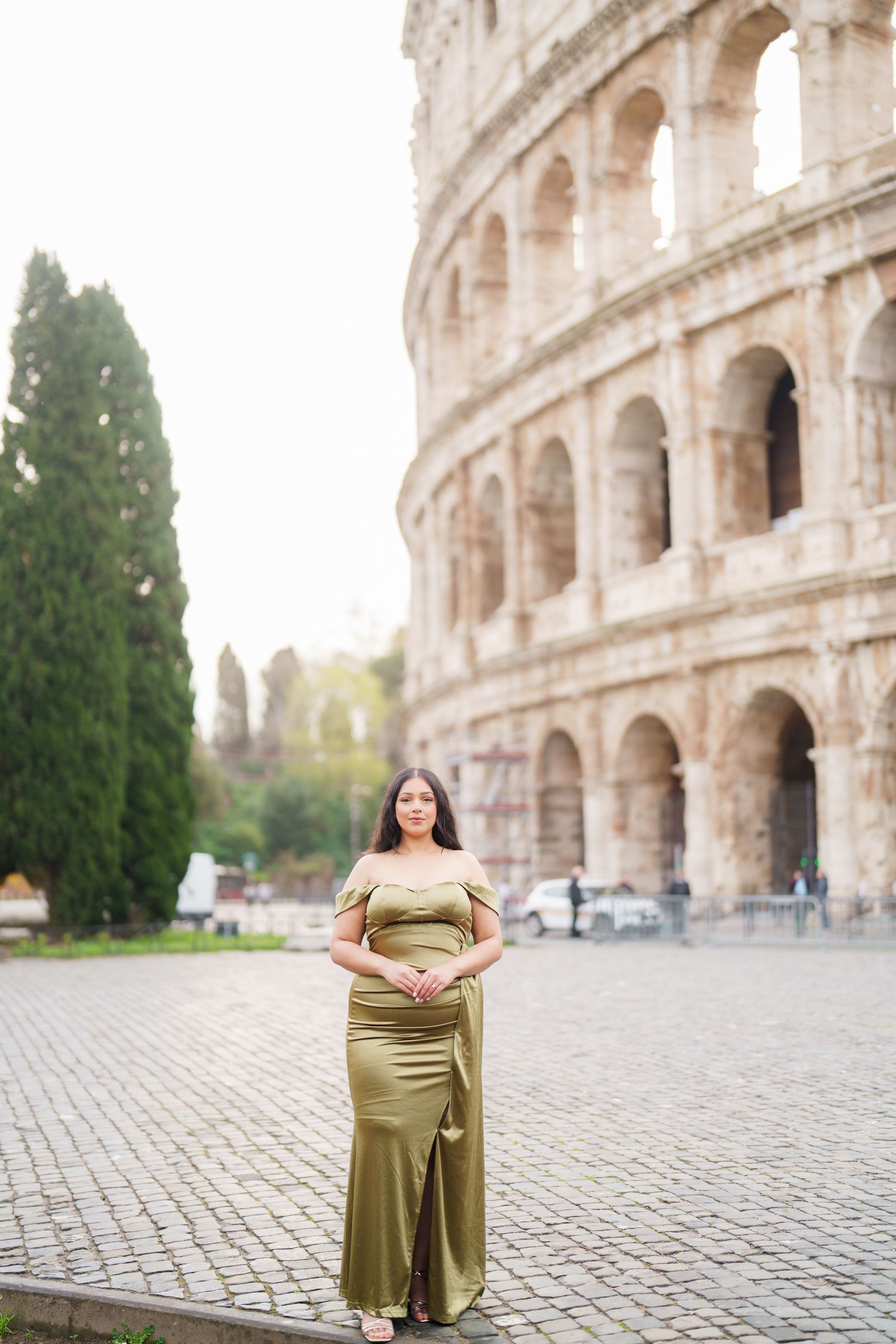 Woman in elegant olive green gown posing in front of the Roman Colosseum in Rome, Italy.
