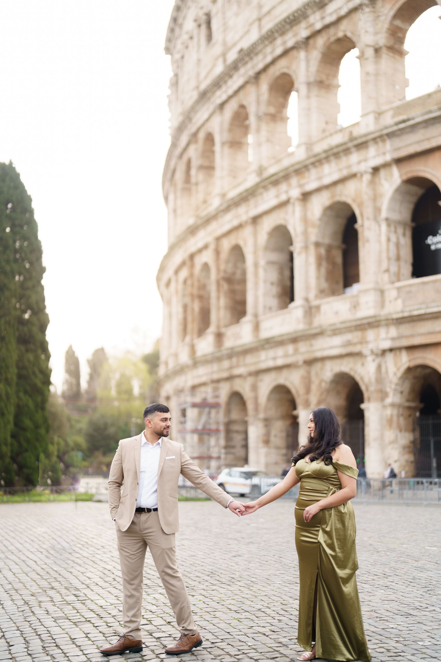Couple holding hands in front of the Colosseum in Rome, woman in green gown, man in beige suit.