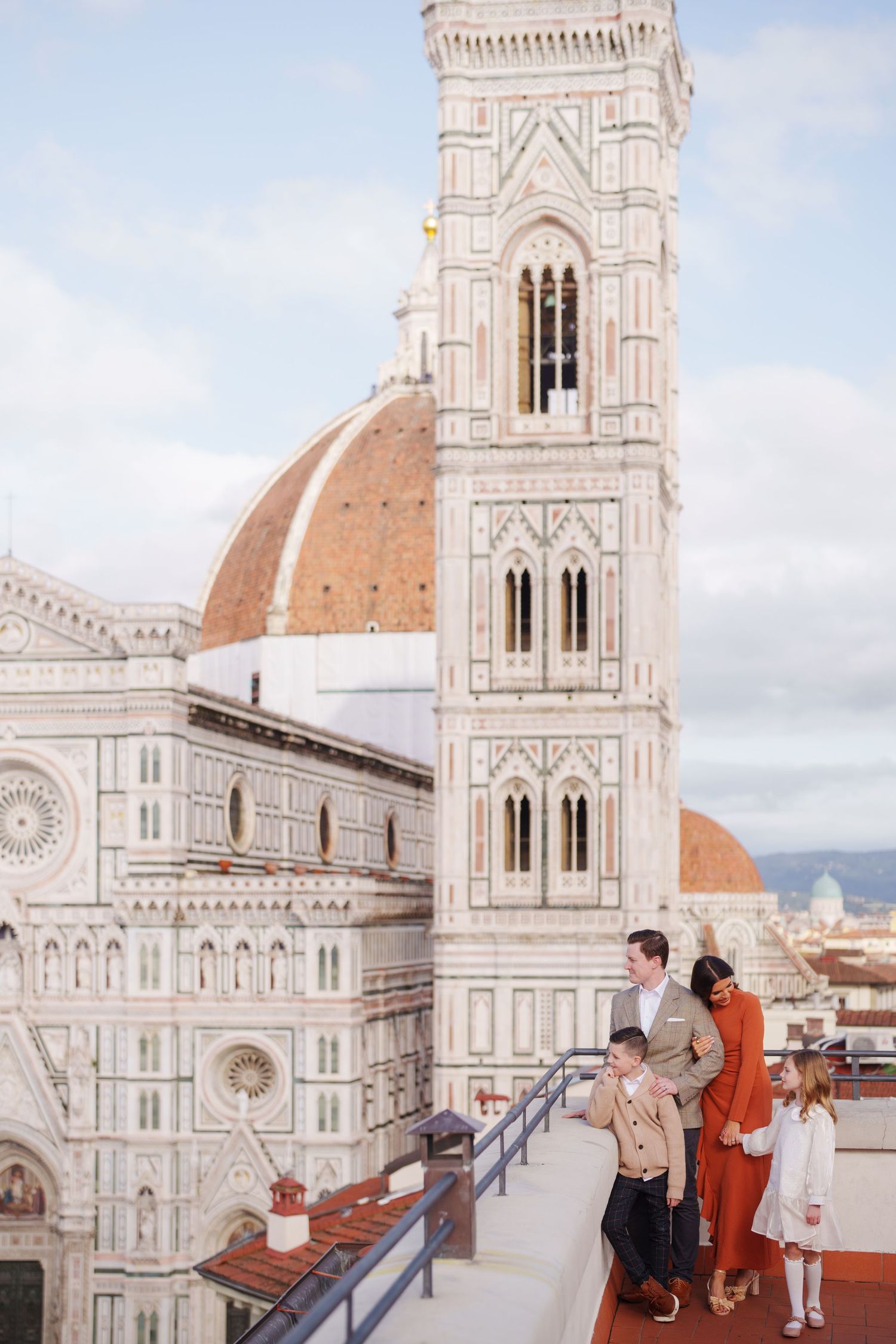 Family posing on a rooftop terrace with Florence Cathedral and Giotto's Campanile in the background, Italy.