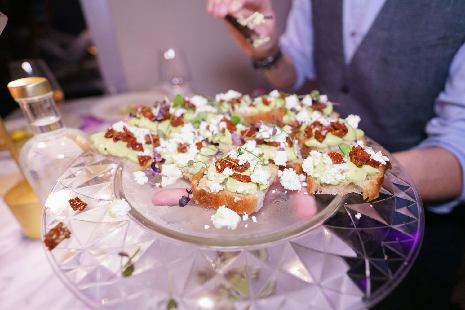 Elegant appetizer platter with bruschetta topped with avocado, goat cheese, and bacon bits served at a catered event.