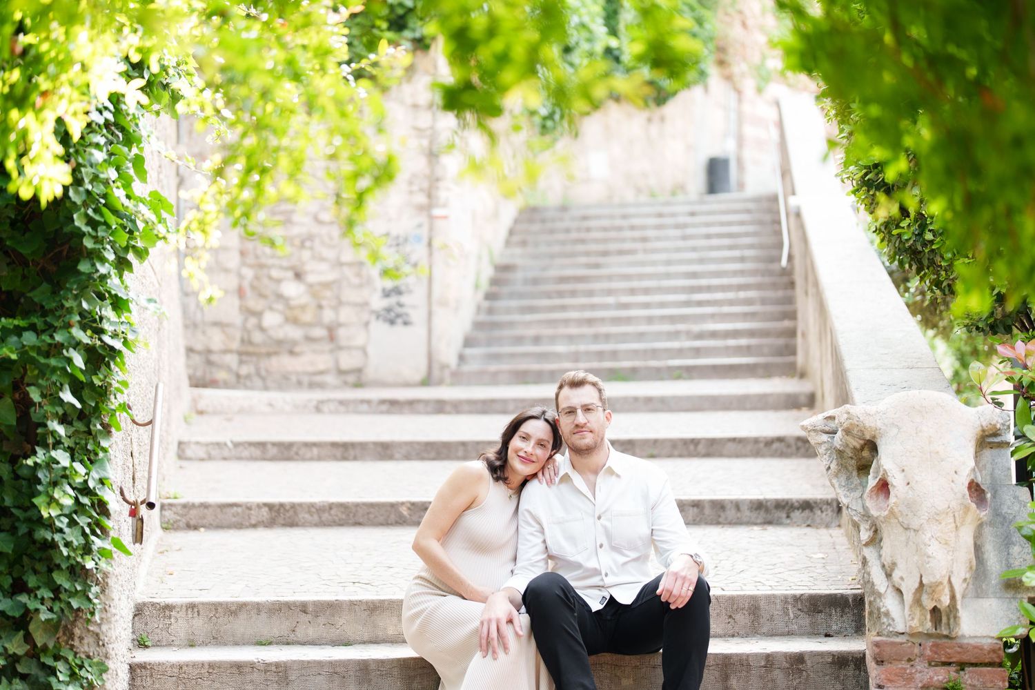 A couple poses together on stone steps surrounded by lush greenery in a romantic outdoor setting.