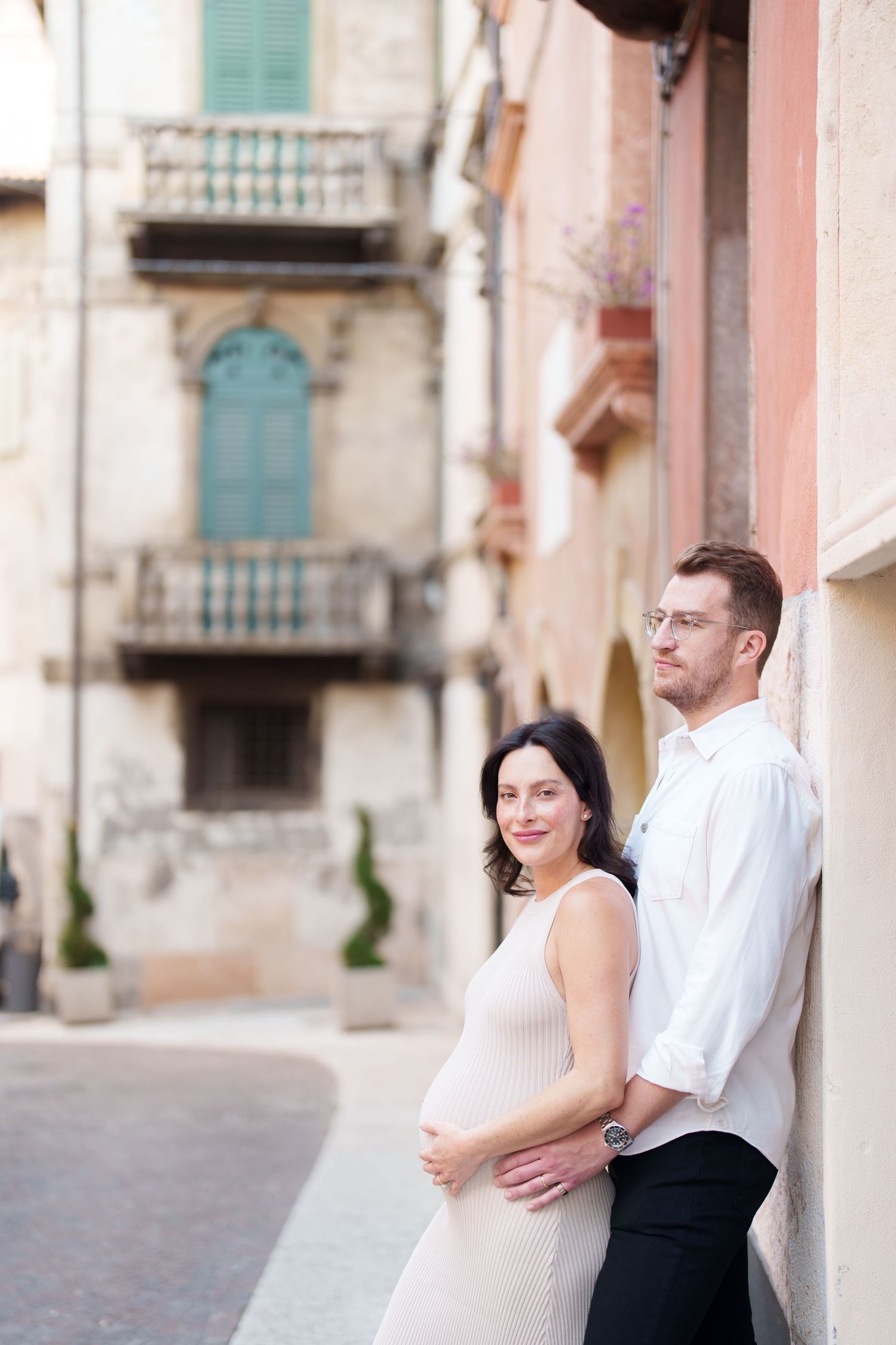 Romantic couple embraces while standing against a Mediterranean style building with turquoise shutters.