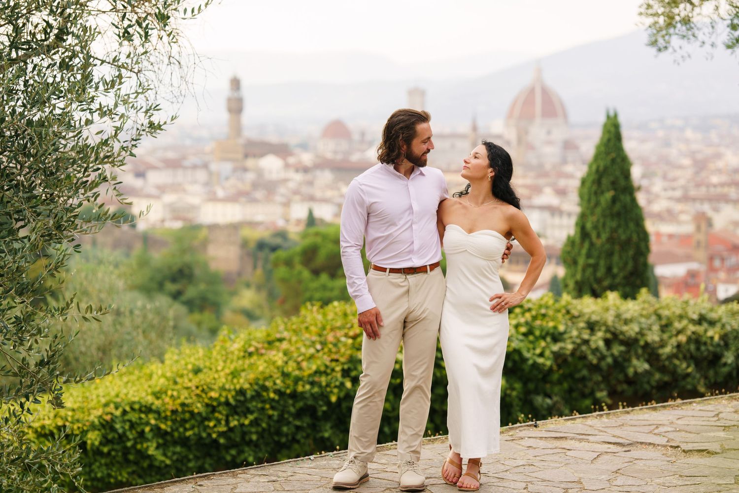 A couple shares a romantic moment overlooking Florence, Italy with the iconic Duomo cathedral visible in the distance.