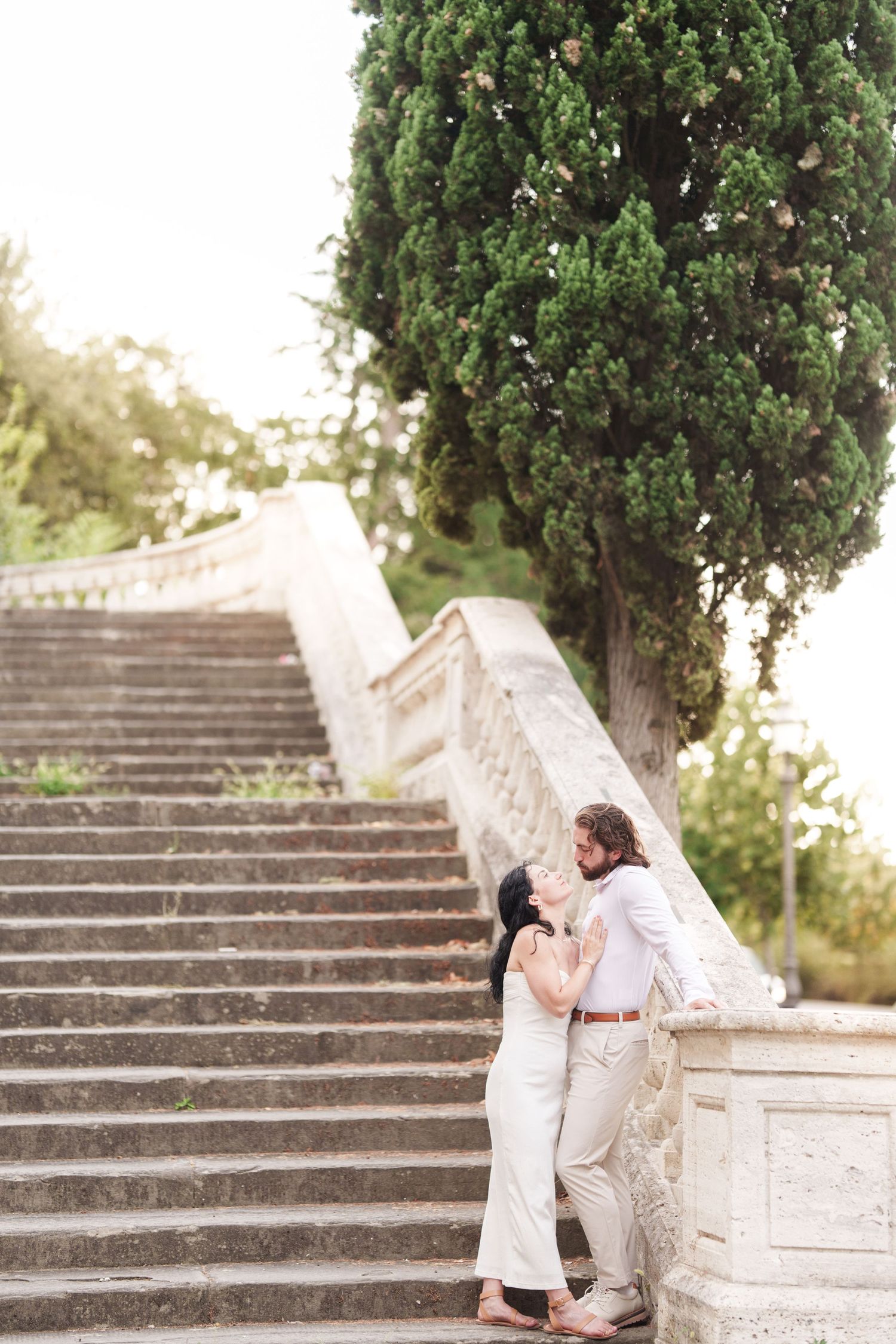 A romantic moment captured on stone stairs surrounded by cypress trees in a Mediterranean garden setting.
