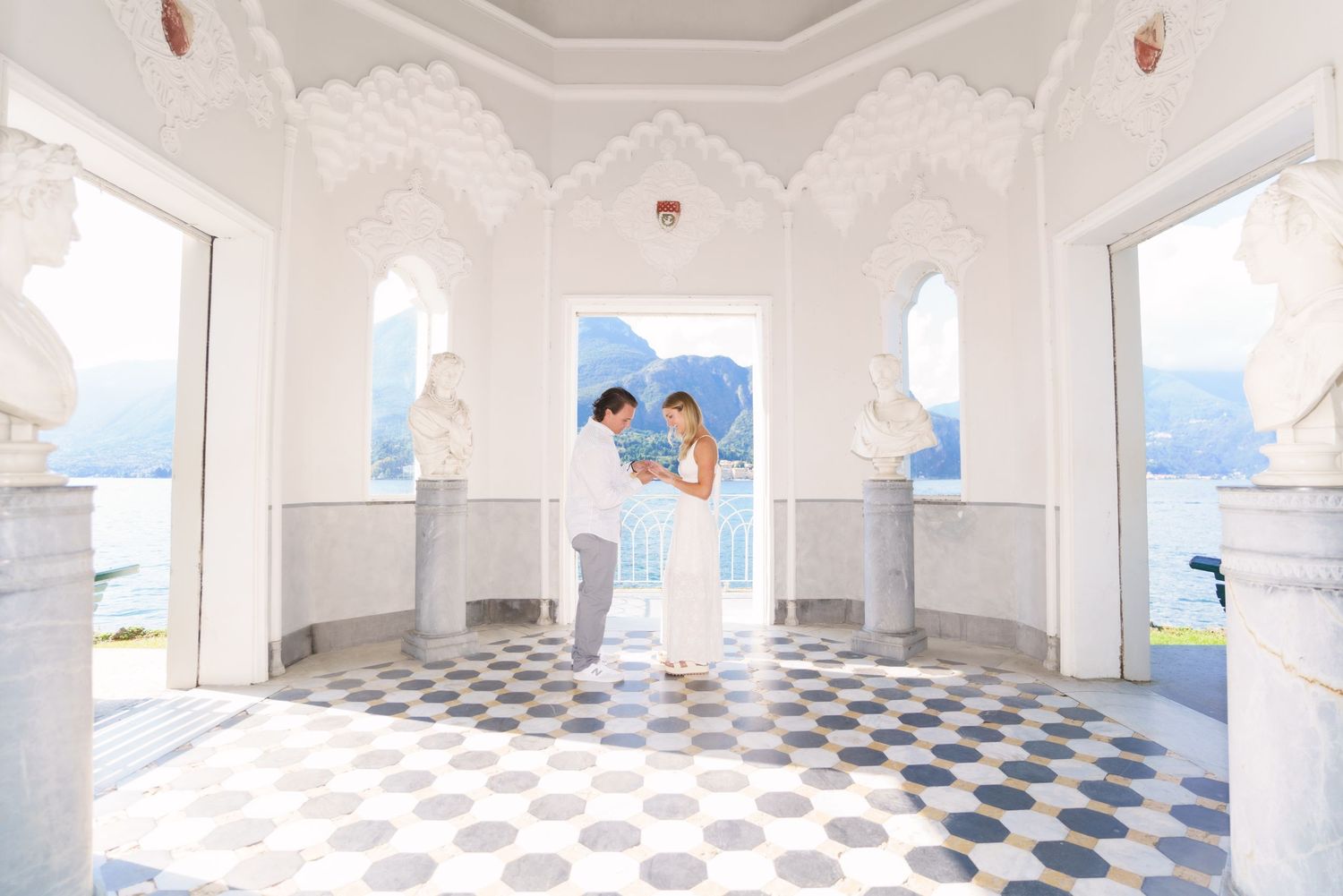 A bright white room with a black and white checkered floor and arched windows overlooking a scenic ocean view.