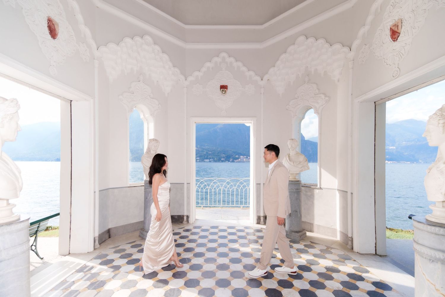 A series of connected white rooms with checkered floors and arched windows overlooking a scenic mountain landscape.