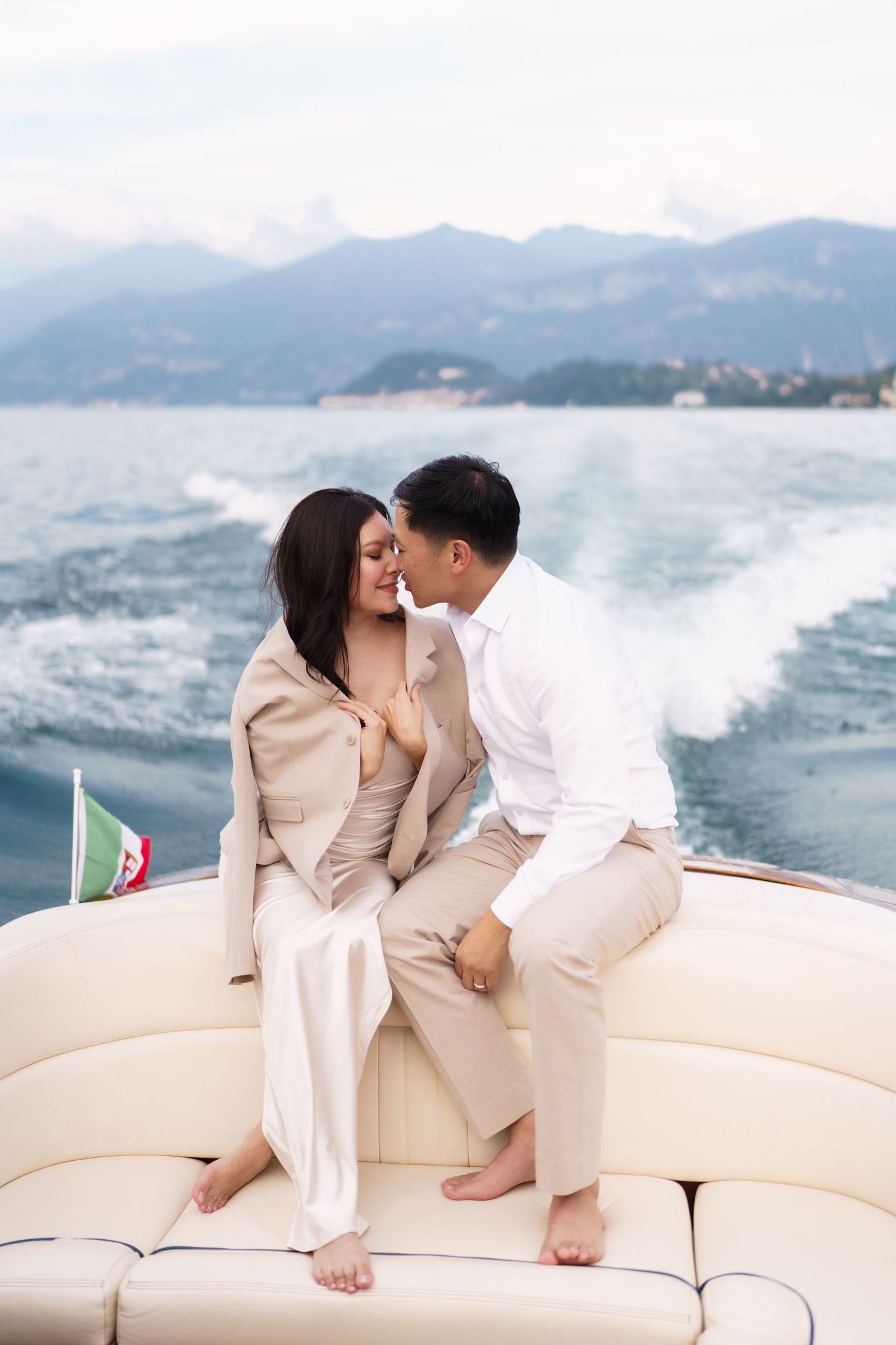 A couple shares an intimate moment on a luxury boat with mountains and ocean waves in the background.