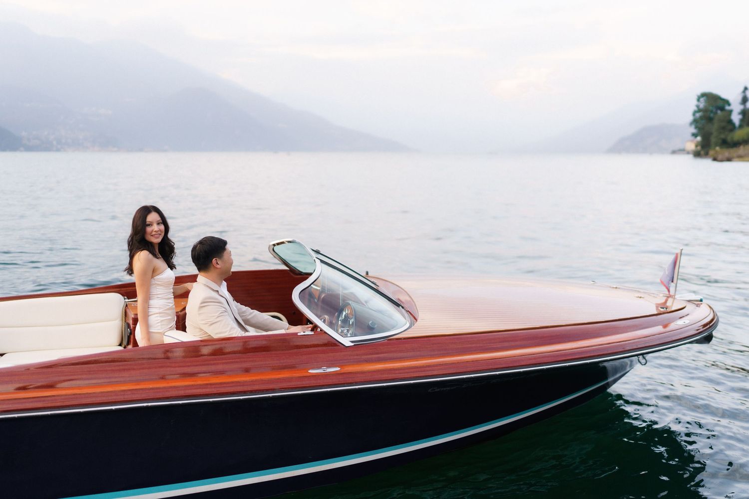 Classic wooden speedboat with polished mahogany hull cruising on calm waters at sunset.