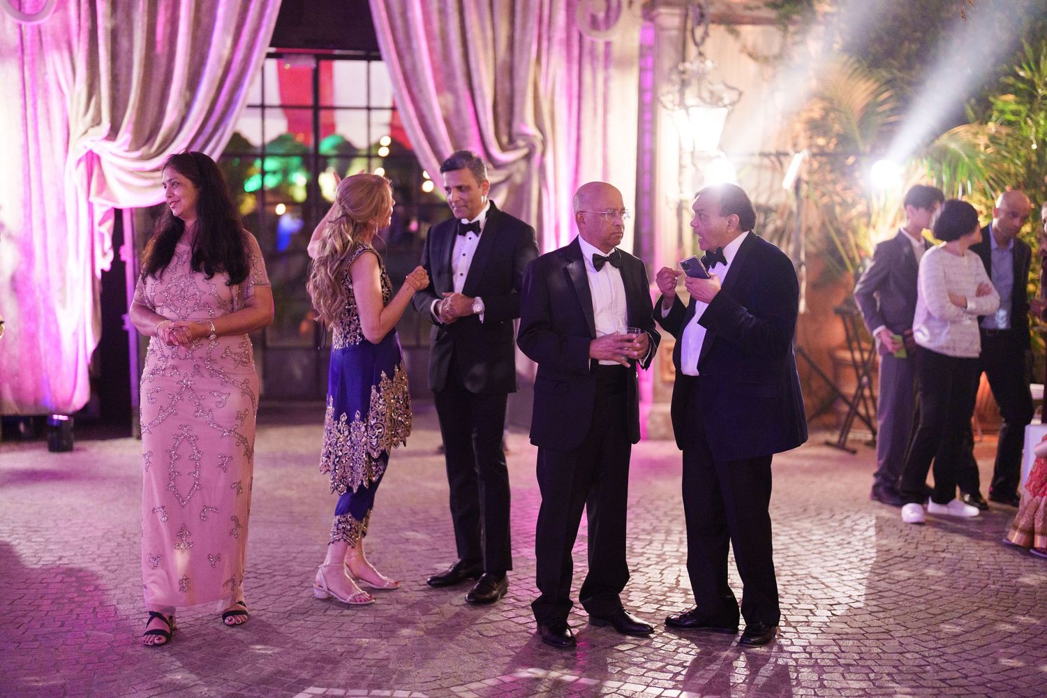 Wedding reception dance floor with guests celebrating under pink and purple lighting.