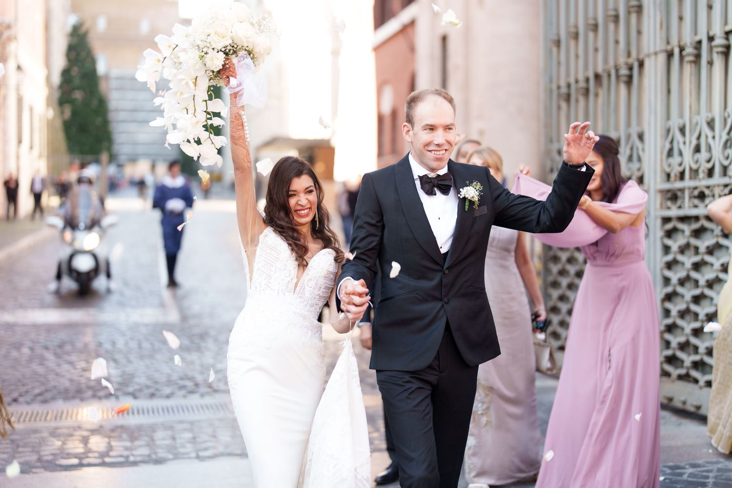 Wedding celebration on a cobblestone street with formal attire and pink bridesmaid dresses.