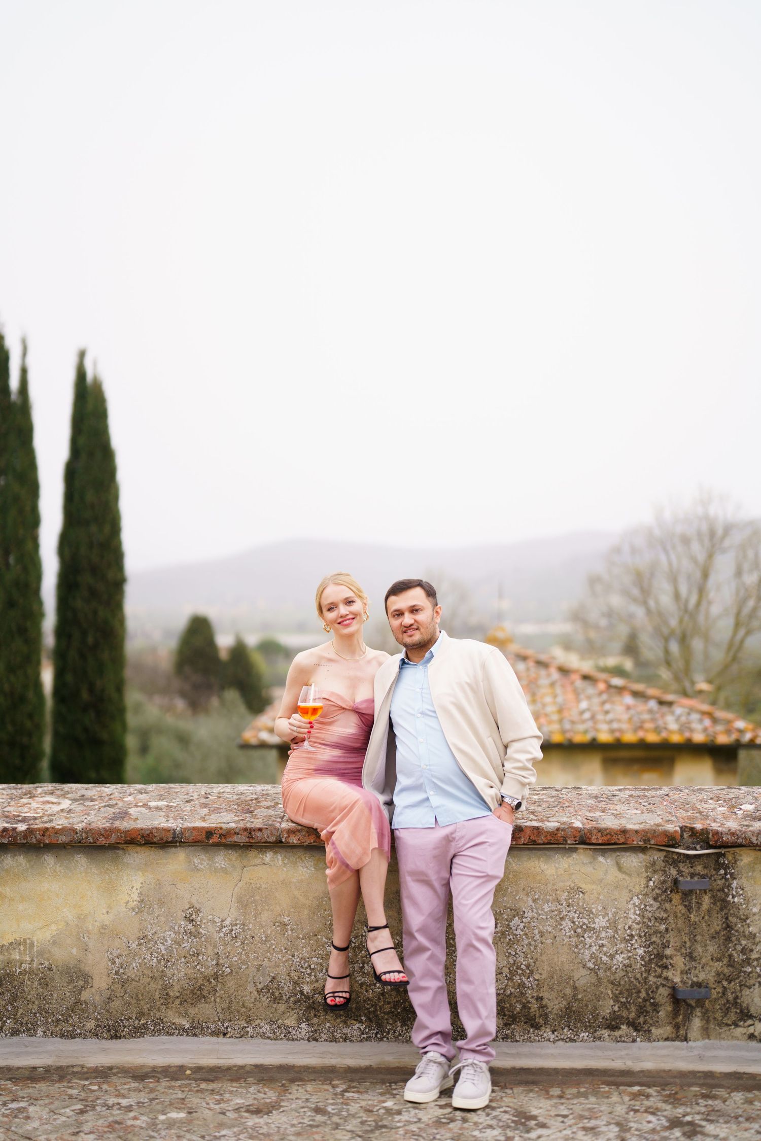 People in pastel outfits pose casually against a stone wall with mountains in the distance.