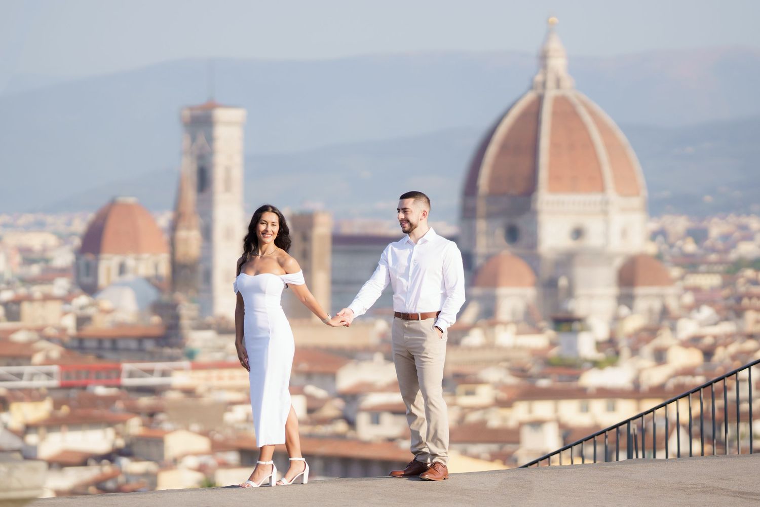 A romantic couple poses at Piazzale Michelangelo overlooking Florence's iconic Duomo and cityscape at sunset.