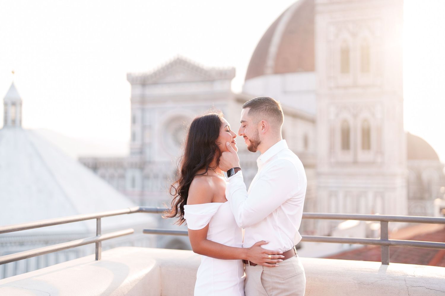 A couple embraces and kisses during a romantic sunset photoshoot in a European city with historic architecture.