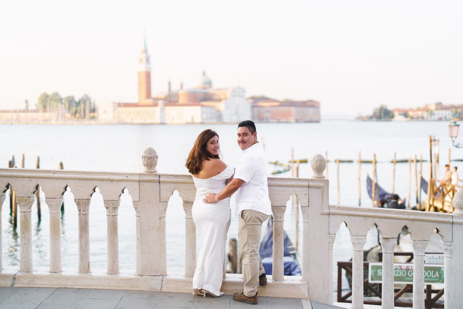Couple enjoying a romantic moment on a white balcony overlooking a scenic Mediterranean cityscape.