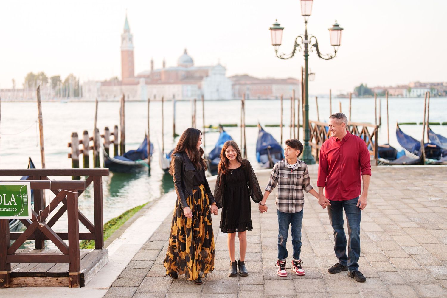 People stroll along the Venice waterfront with gondolas and the iconic San Giorgio Maggiore church in the background.
