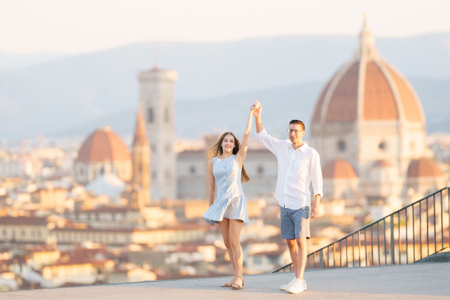 photographer Florence Couple walking hand in hand along a scenic viewpoint overlooking Florence's historic skyline with Duomo cathedral.