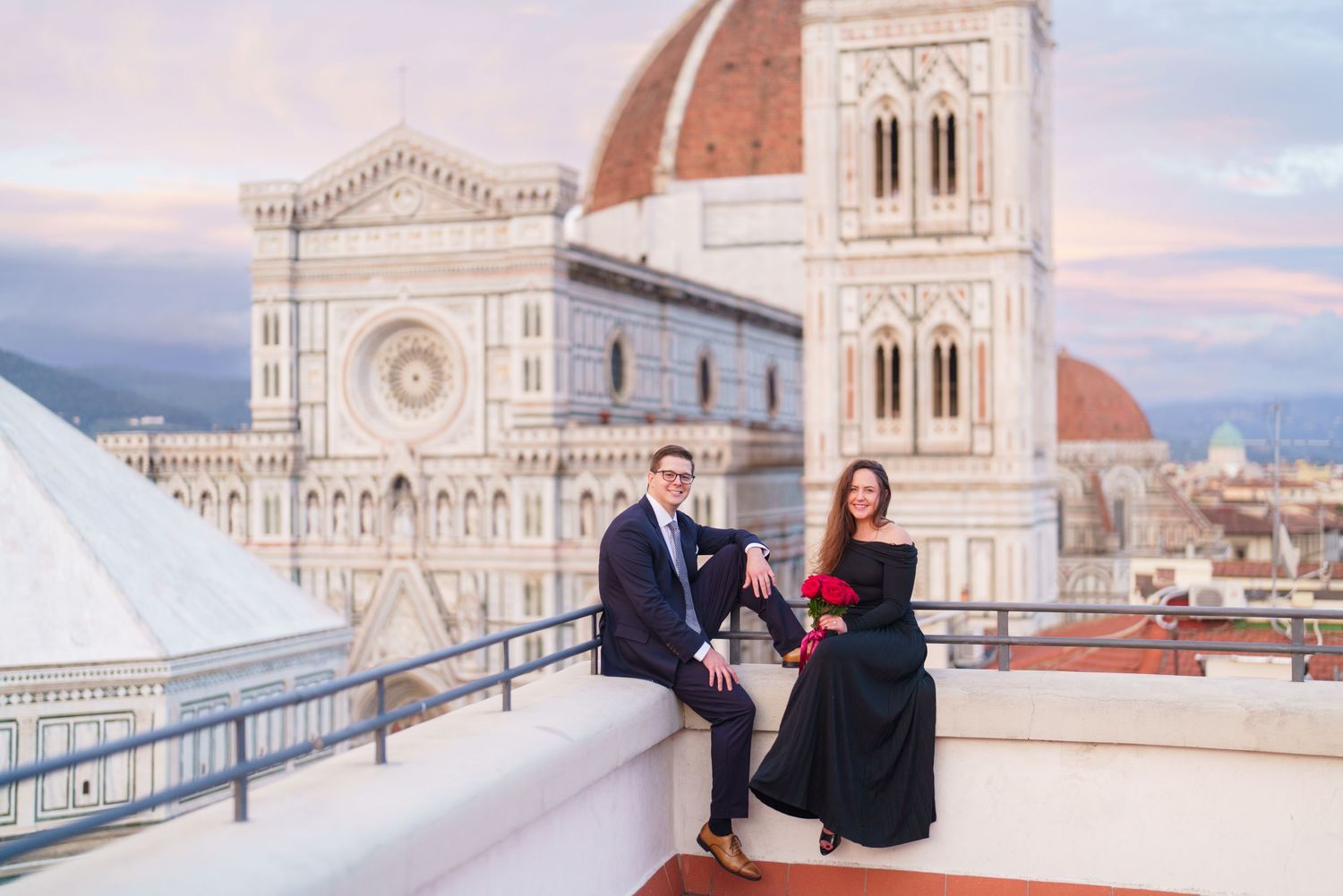 Couple shares a romantic moment on a terrace overlooking the historic Florence Cathedral and cityscape at sunset.