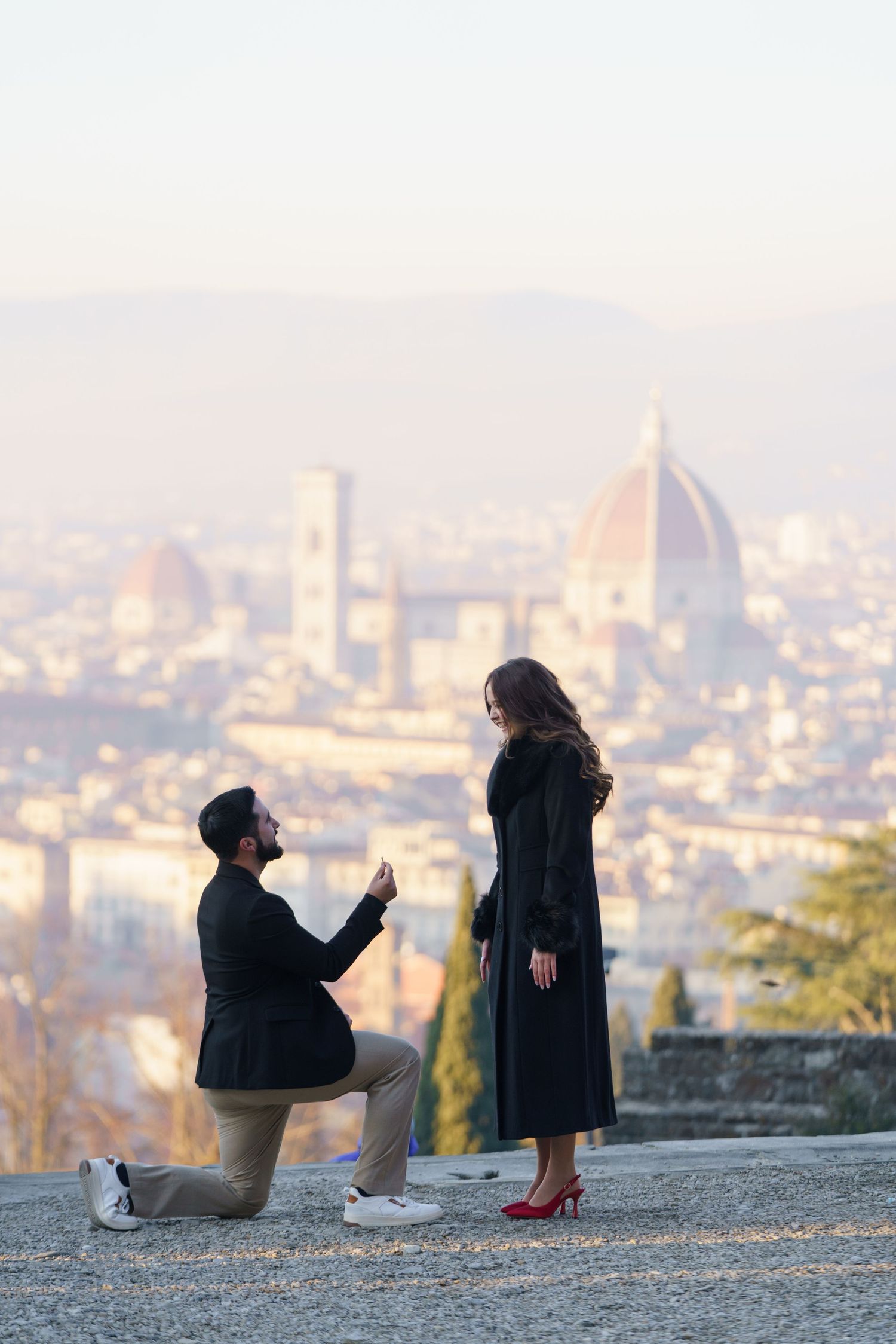 Silhouettes of people sitting on a hillside overlook the Florence cityscape at sunset with the Duomo visible in the distance.