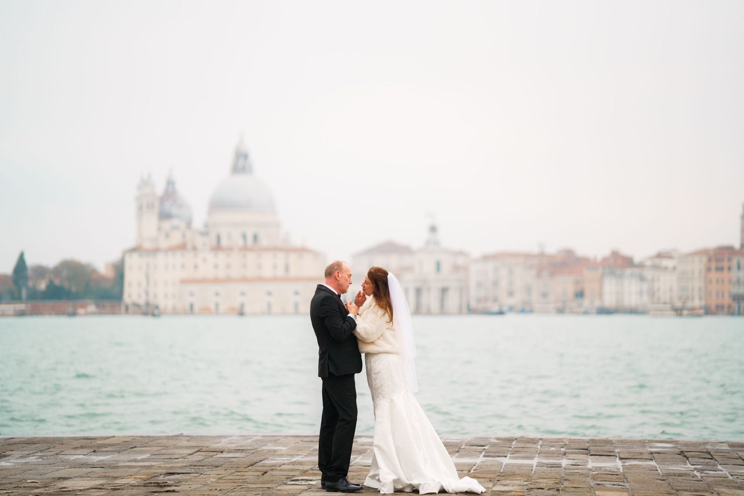 A couple shares a romantic moment along the Venice waterfront with Santa Maria della Salute church in the background.