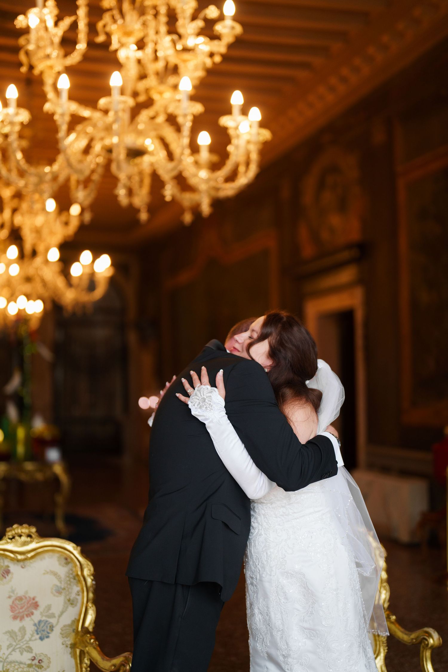 Romantic couple shares a kiss under ornate crystal chandeliers in an elegant ballroom setting during their wedding celebration.