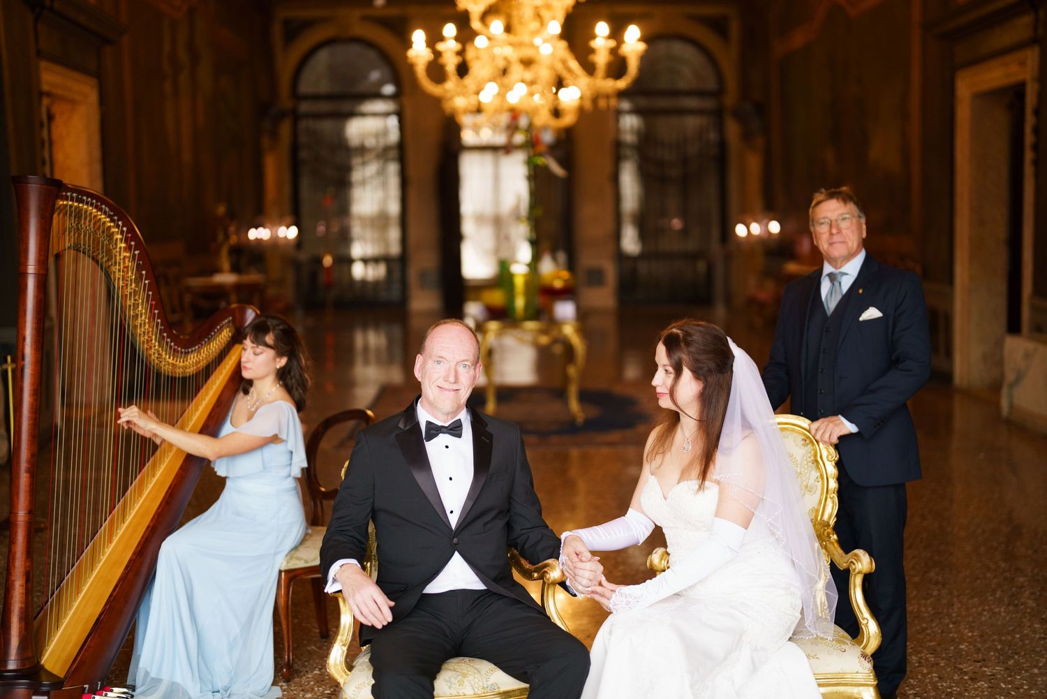 Elegant wedding celebration in an ornate ballroom with a harp player, formal attire, and chandelier lighting.