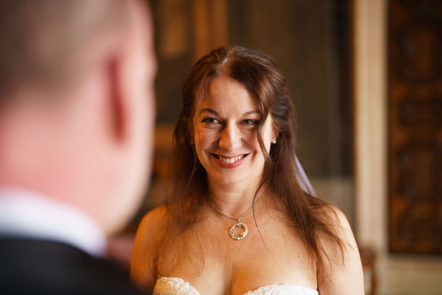 A bride shares a joyful moment with someone during a wedding celebration in a warmly lit indoor setting.