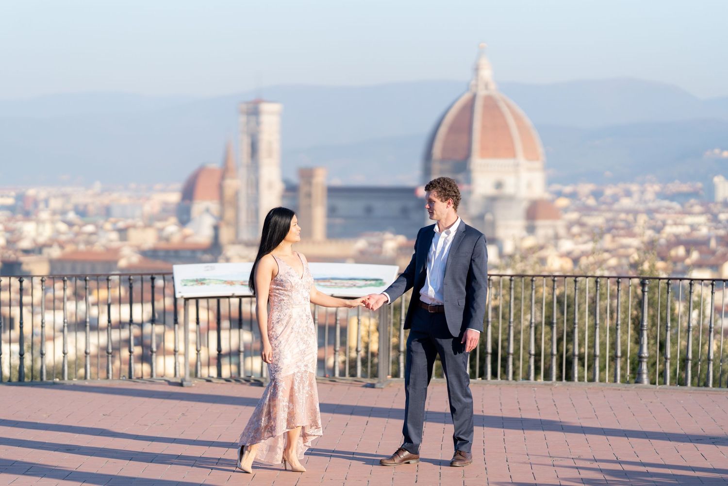 A couple stands at Piazzale Michelangelo viewpoint overlooking Florence's iconic Duomo cathedral and cityscape at sunset.