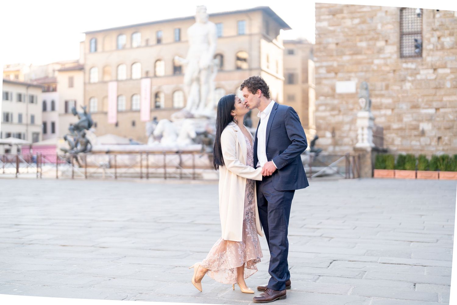 A romantic couple shares a tender moment in a beautiful Italian plaza with historic architecture in the background.