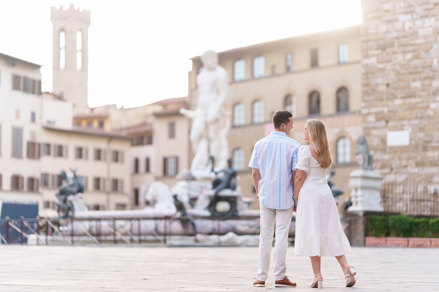 A couple in white outfits walks hand in hand through the historic streets of Florence, Italy near Palazzo Vecchio.