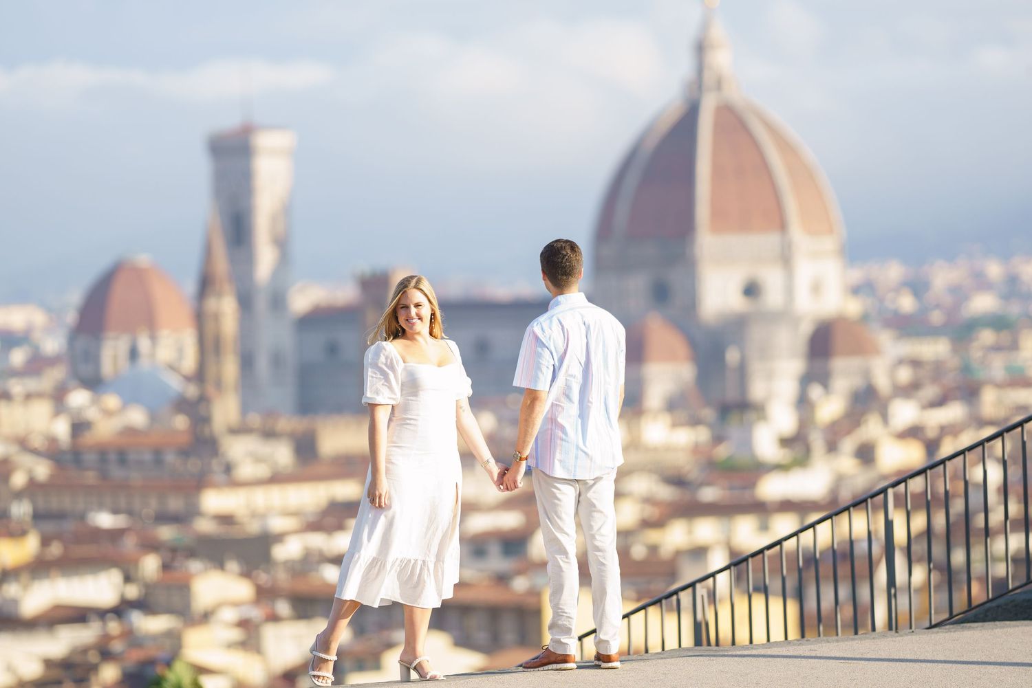 Couple in white outfits walking up stone steps overlooking Florence cityscape with Duomo cathedral in background.