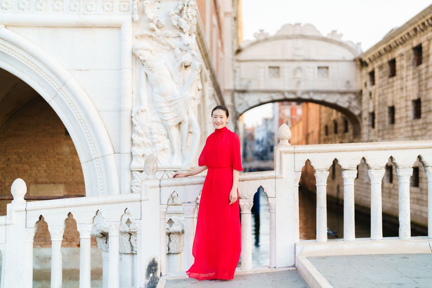 Woman in red gown poses near Bridge of Sighs in Venice, Italy.
